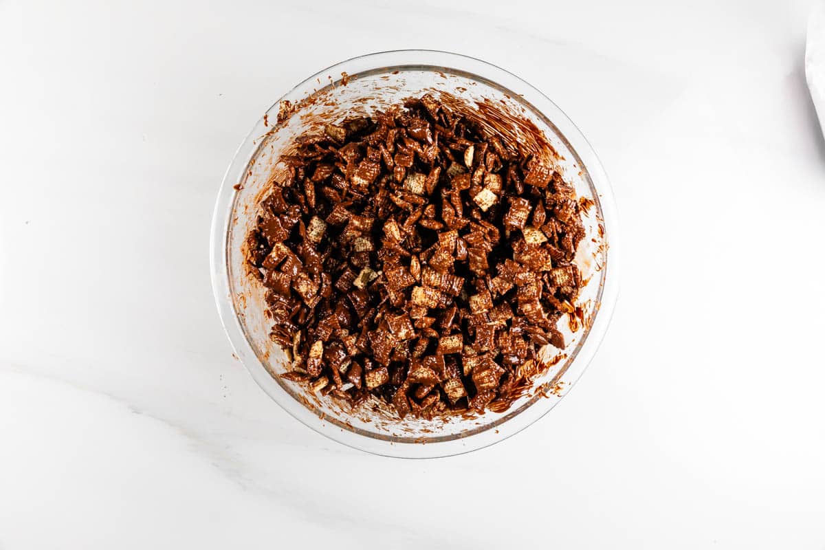 A glass bowl filled with a chocolatey, chunky mixture on a white surface.