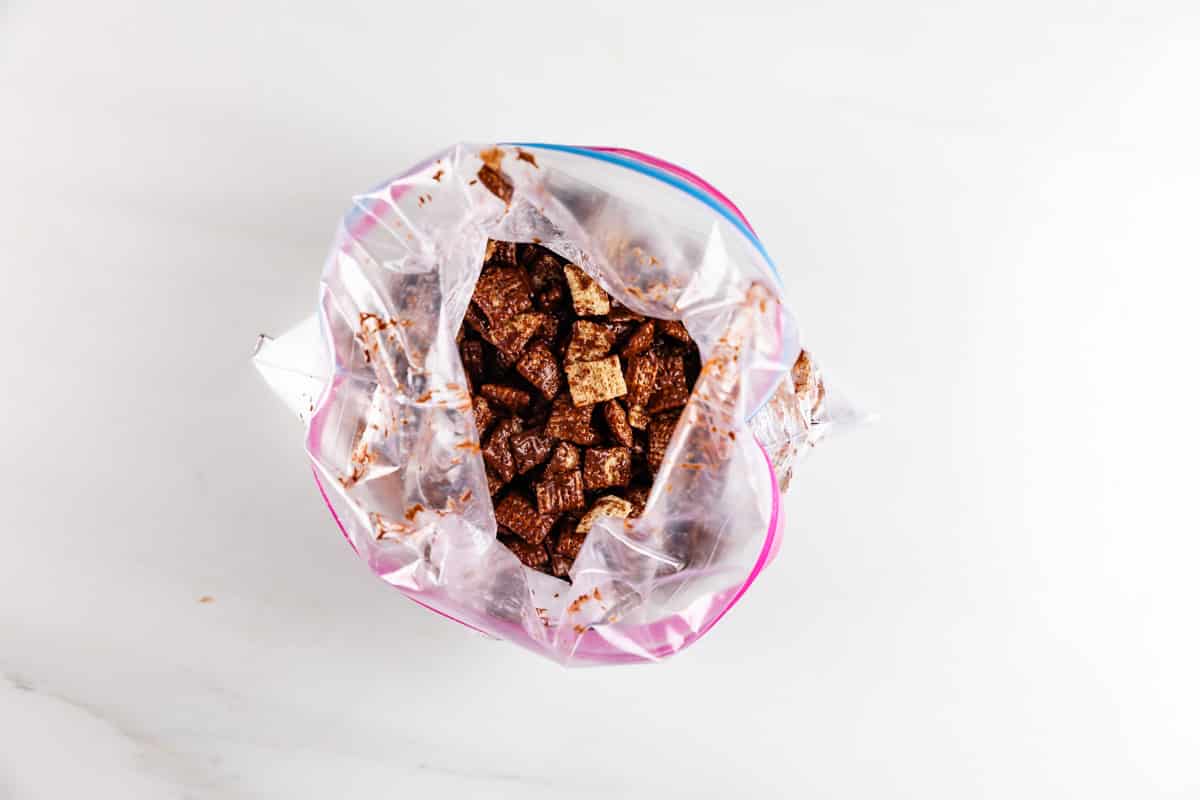 A clear plastic ziplock bag filled with chocolate-coated cereal squares on a white surface.