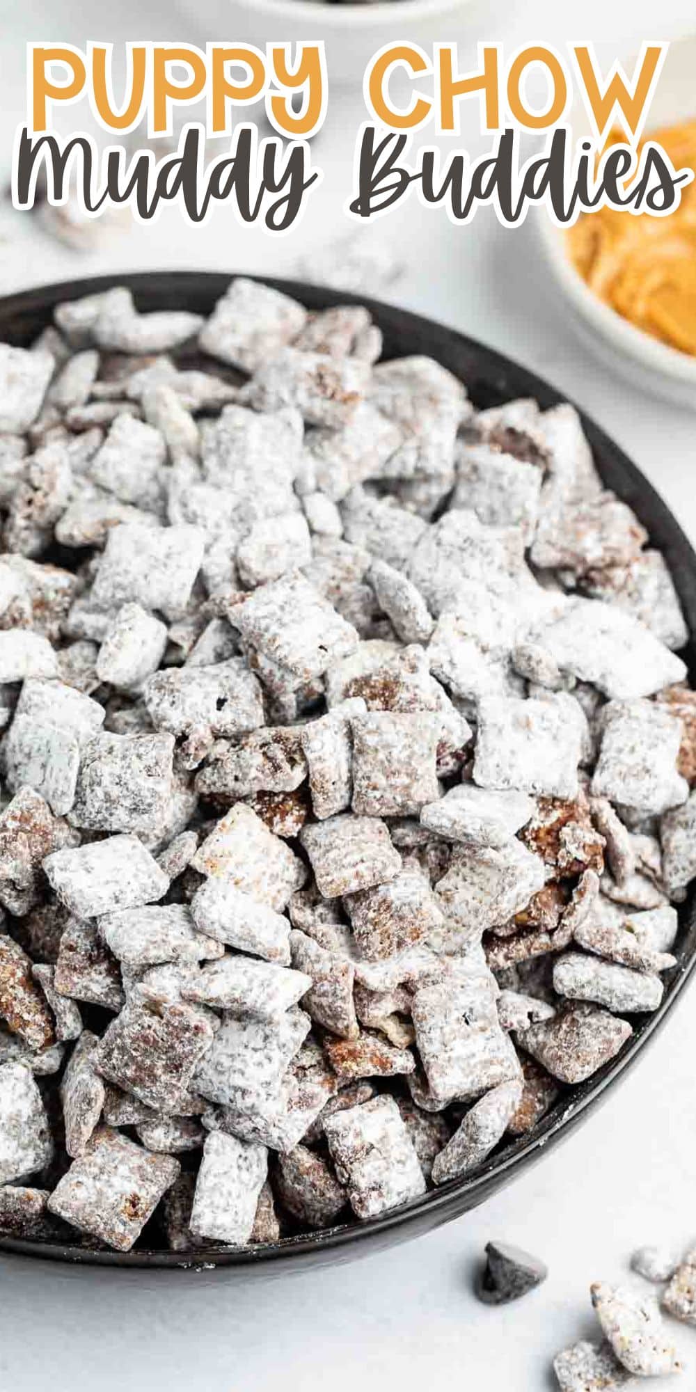 A plate filled with Puppy Chow or Muddy Buddies, consisting of cereal pieces coated in chocolate, peanut butter, and powdered sugar. A bowl of peanut butter is visible in the background.