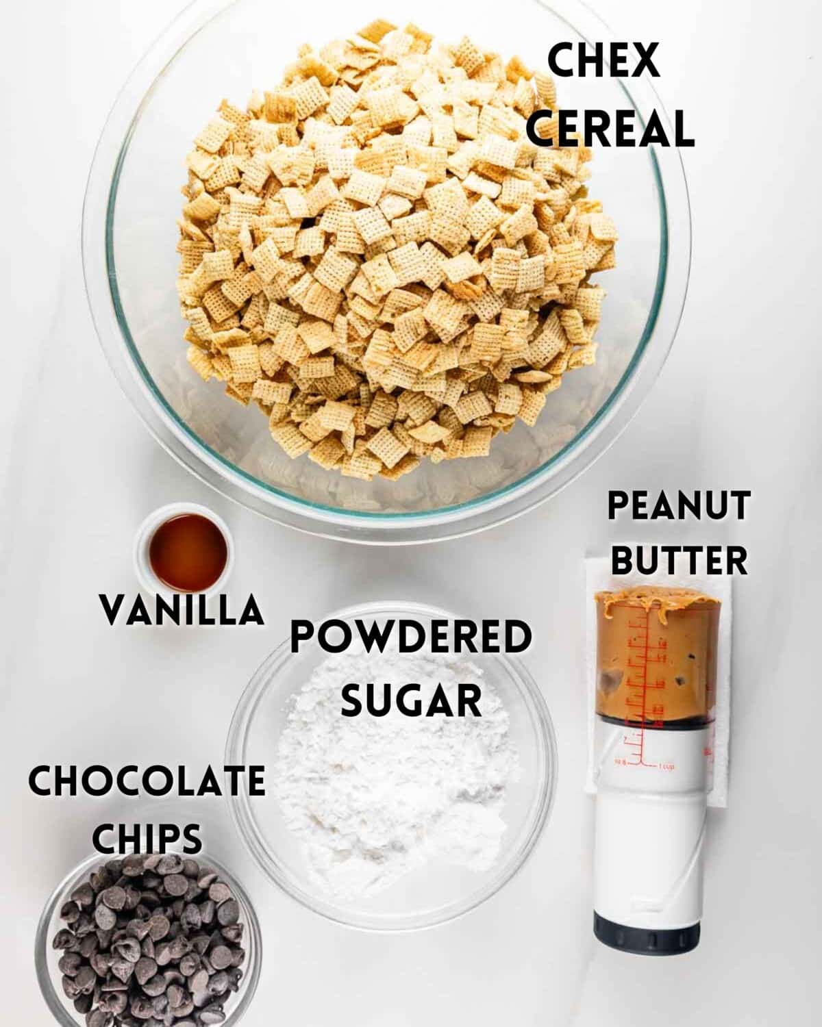 Ingredients for making a snack mix are arranged on a white surface, including Chex cereal in a glass bowl, a cup of vanilla extract, a bowl of chocolate chips, powdered sugar, and a container of peanut butter.