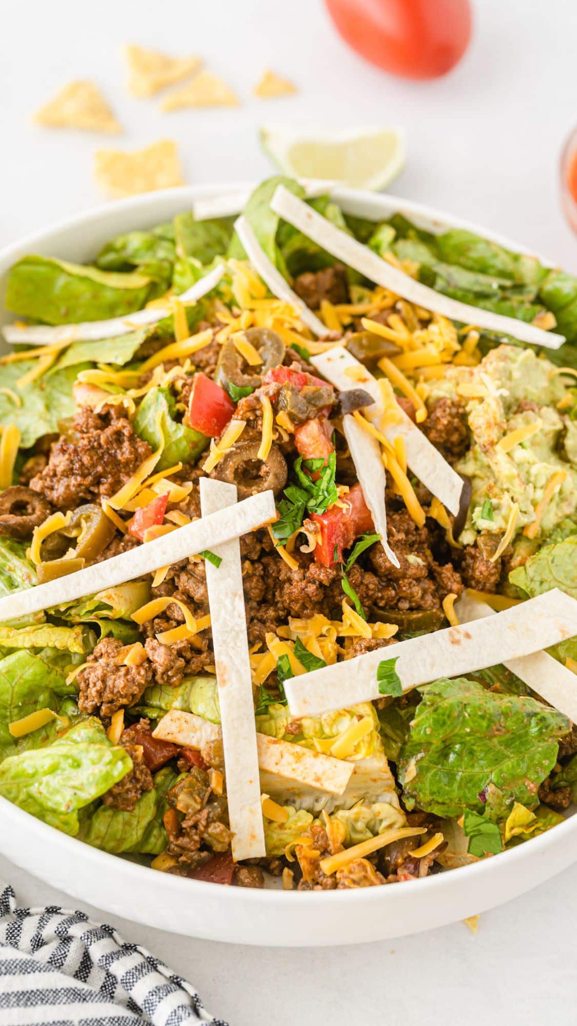 taco salad in a white bowl topped with meat and sauces.