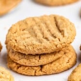 A stack of three 3 ingredient peanut butter cookies with a crisscross pattern on top, surrounded by more cookies on a white surface.