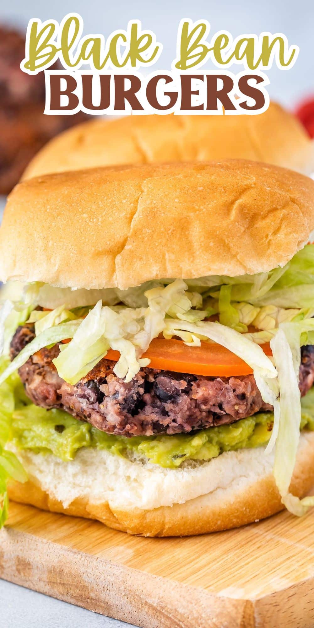 Close-up of a black bean burger on a wooden board. The burger has a bun, black bean patty, sliced tomato, lettuce, and a layer of green spread. Text at the top reads Black Bean Burgers.