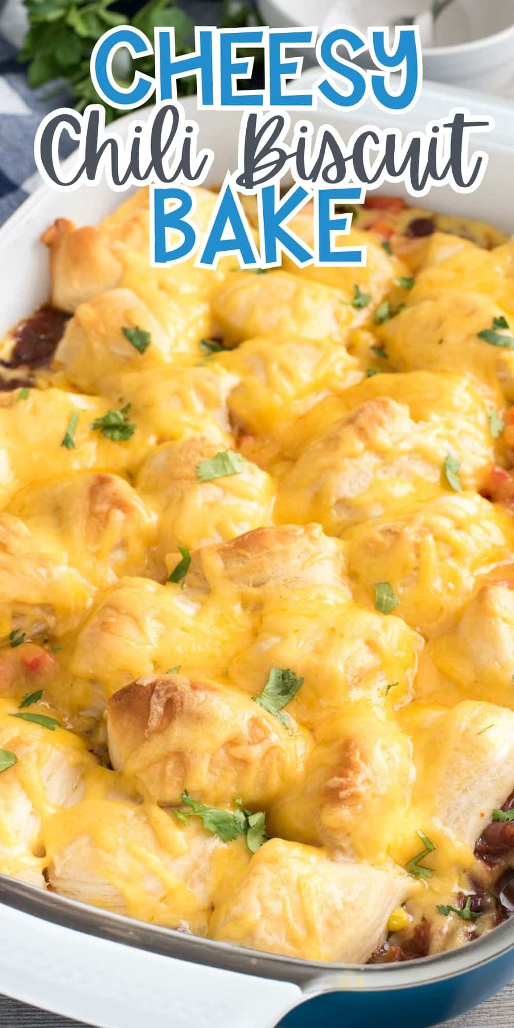 A baking dish filled with a cheesy chili biscuit bake. The top is covered with melted cheese and garnished with chopped herbs. The dish is golden brown with biscuit pieces visible. Text at the top reads Cheesy Chili Biscuit Bake.