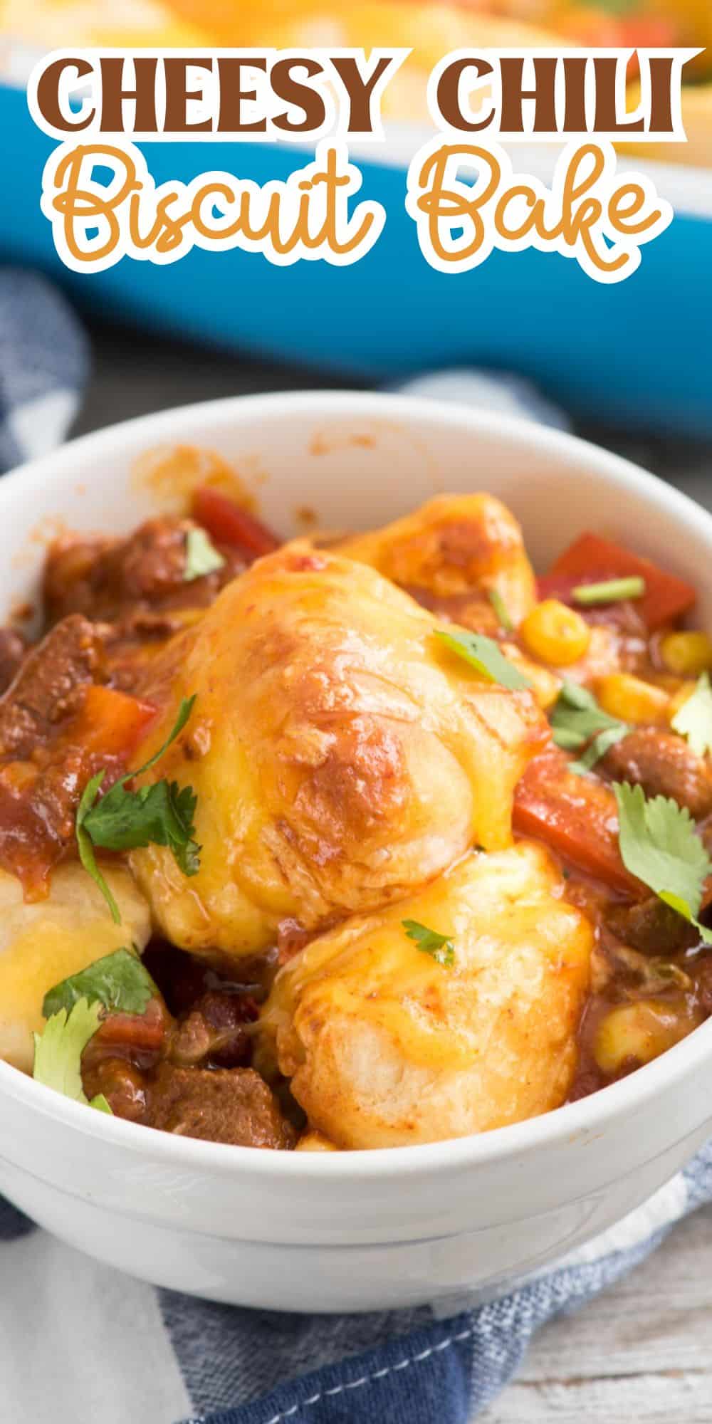 A bowl filled with cheesy chili biscuit bake, featuring biscuits topped with melted cheese, ground meat, corn, and garnished with cilantro. The text above the dish reads Cheesy Chili Biscuit Bake in bold letters.