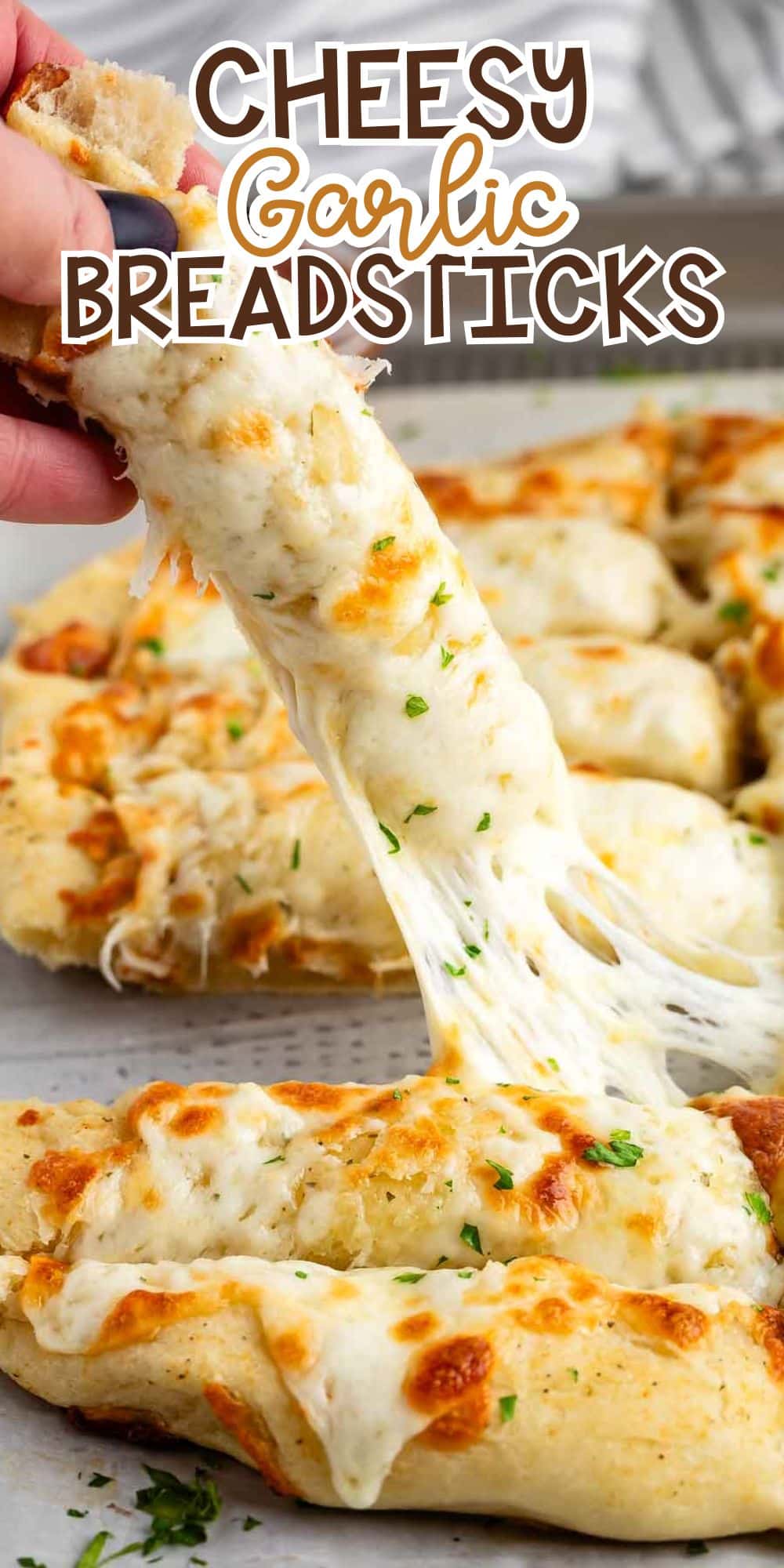 A hand pulling apart a cheesy garlic breadstick with melted cheese stretching. The breadsticks are topped with herbs and arranged on a baking sheet. The text Cheesy Garlic Breadsticks is at the top.
