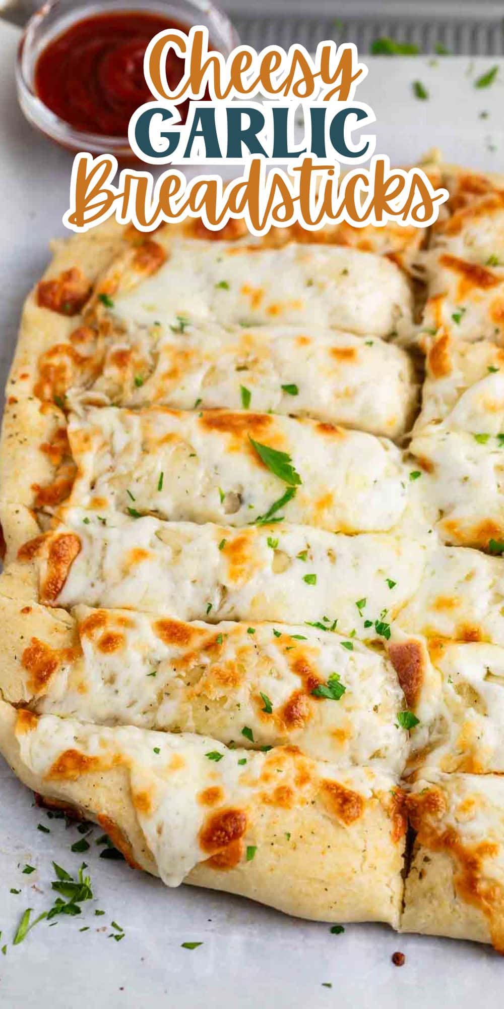 Cheesy garlic breadsticks topped with melted cheese and herbs, cut into sections. A small bowl of red marinara sauce sits in the background. Text overlay reads Cheesy Garlic Breadsticks.
