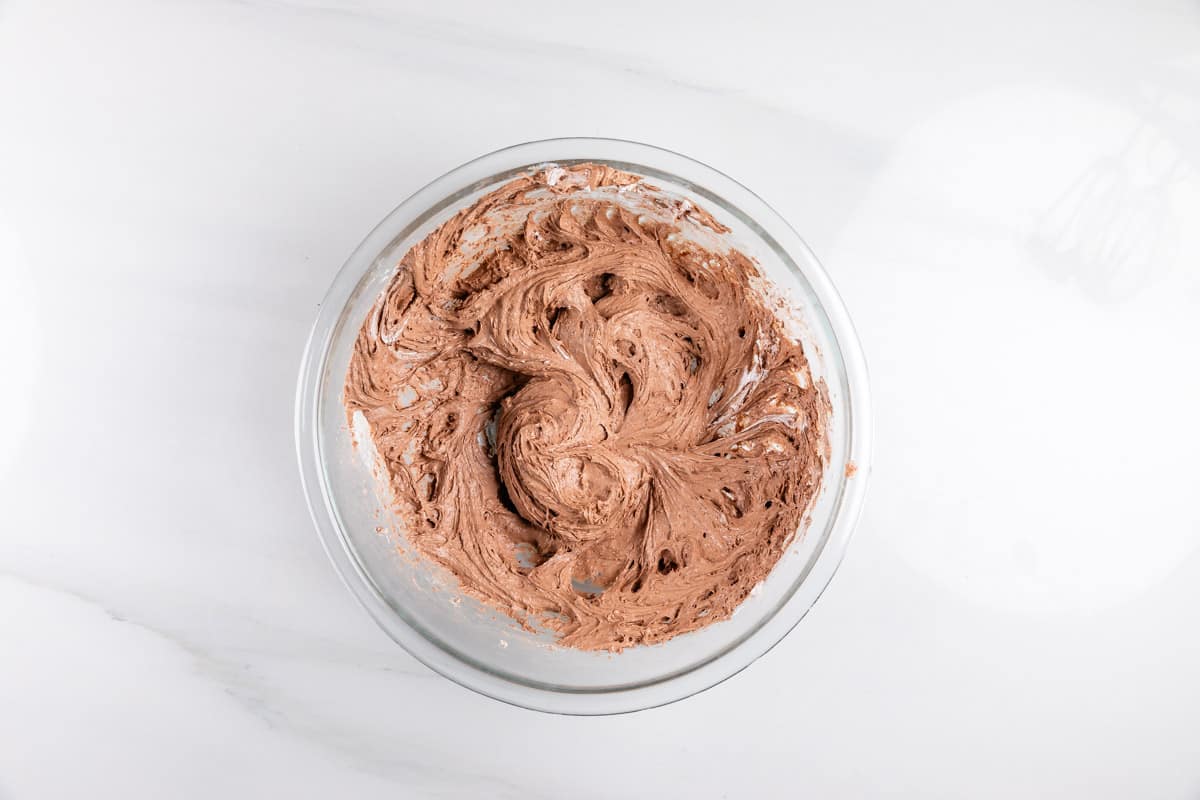 A clear glass bowl filled with swirled chocolate cake batter sits on a white marble surface.