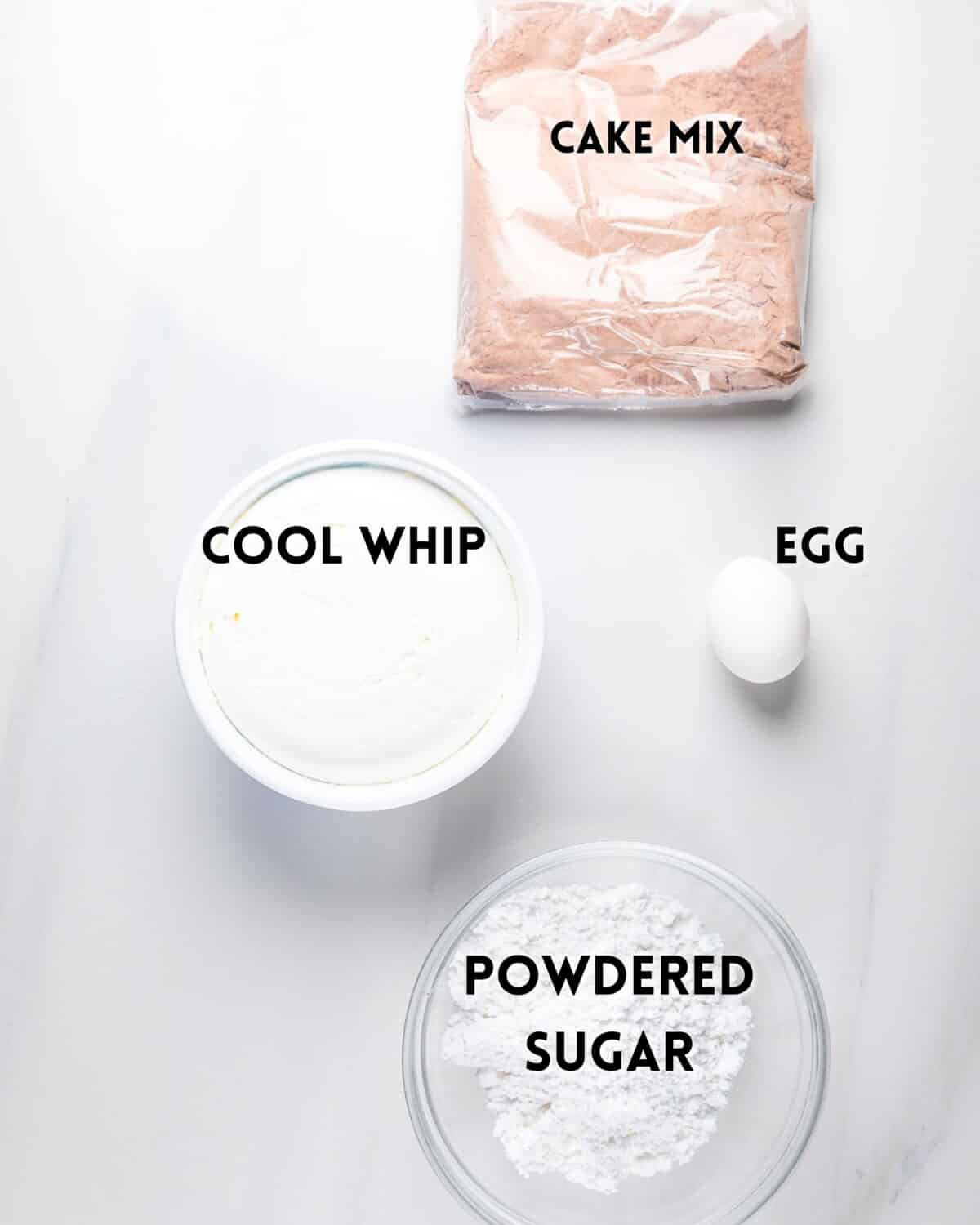A top-down view of four baking ingredients: a sealed bag of cake mix, a container of Cool Whip, a single egg, and a bowl of powdered sugar, all labeled on a white surface.