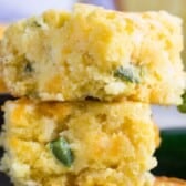 Two pieces of Mexican cornbread stacked on top of each other, with visible bits of green jalapeño pepper embedded in the moist, crumbly texture.