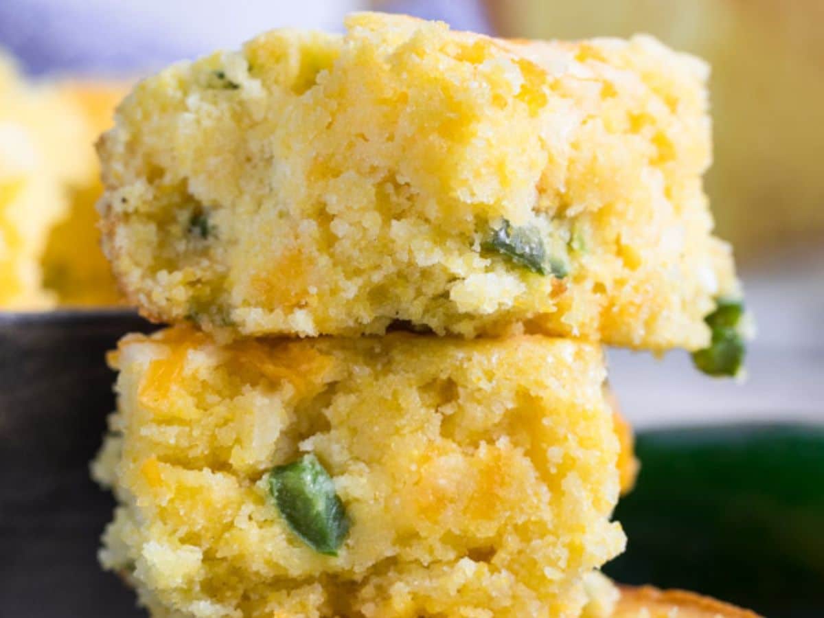 Two pieces of Mexican cornbread stacked on top of each other, with visible bits of green jalapeรฑo pepper embedded in the moist, crumbly texture.