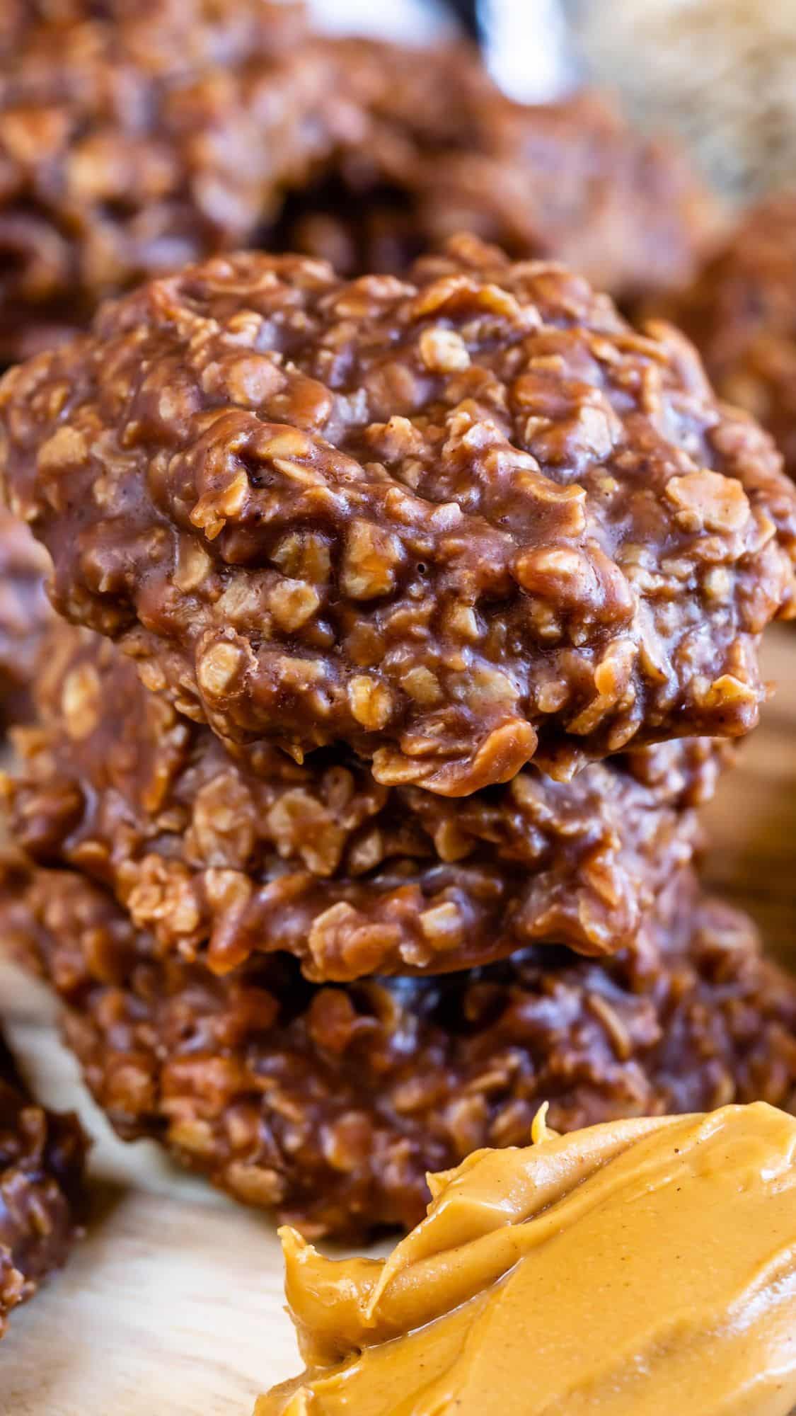 A close-up of stacked no-bake chocolate oatmeal cookies with a dollop of creamy peanut butter in the foreground.