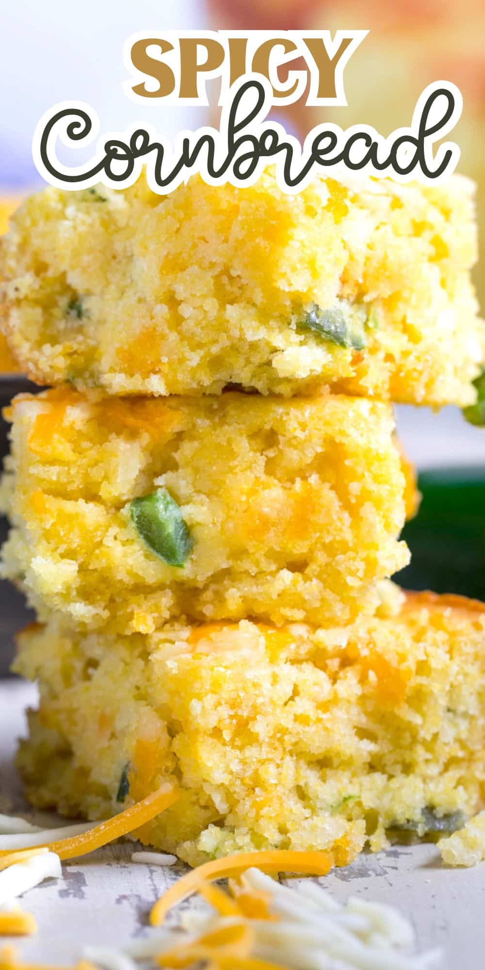 Three pieces of spicy cornbread are stacked, showcasing a golden texture with visible green and orange bits, likely jalapeño and cheese. The text Spicy Cornbread is at the top, and some shredded cheese is scattered around.