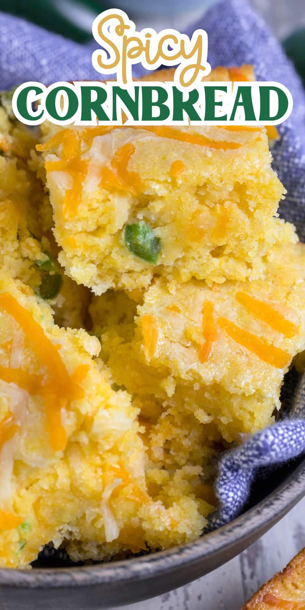 Slices of spicy cornbread topped with melted cheese and green peppers are stacked in a dark, textured bowl lined with a blue cloth. The words Spicy Cornbread appear at the top in stylized text.