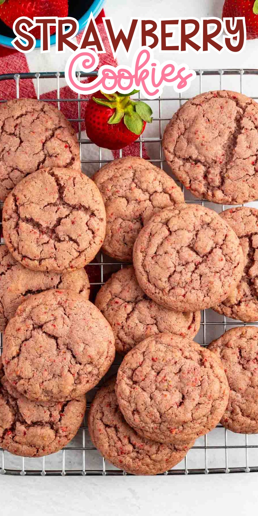 A cooling rack with a dozen pink strawberry cookies sits on a white surface. A fresh strawberry is placed near the cookies. The text Strawberry Cookies appears at the top of the image.