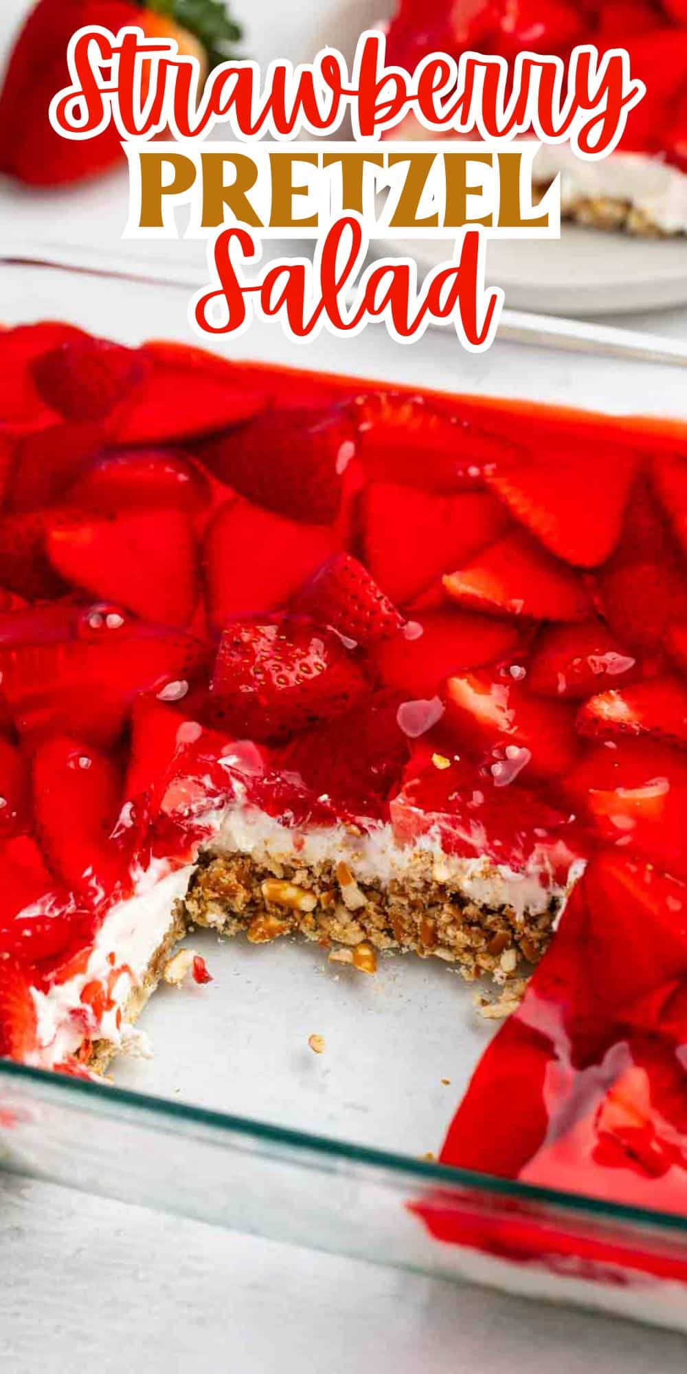 A glass dish of strawberry pretzel salad with a slice removed, revealing layers of crushed pretzels, creamy filling, and strawberry gelatin topping. Text on the image reads Strawberry Pretzel Salad.