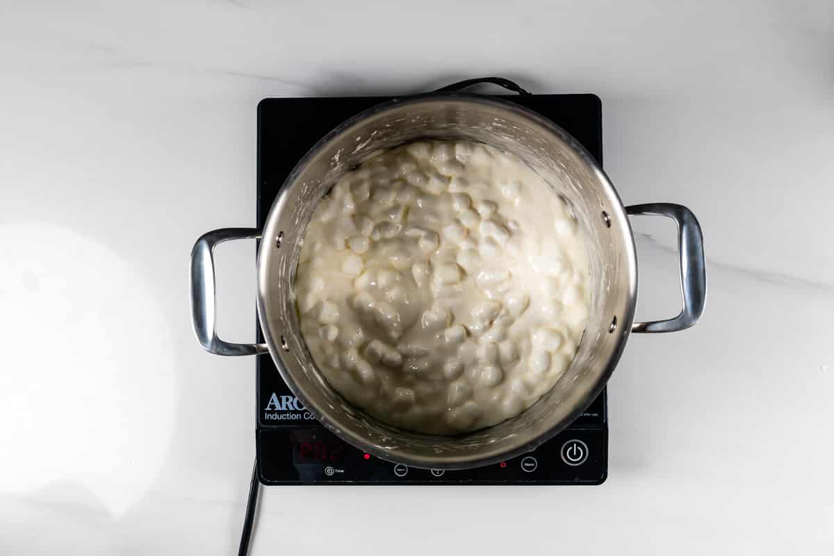 Overhead view of a pot filled with gnocchi in a creamy white sauce, sitting on a black electric cooktop on a white surface.