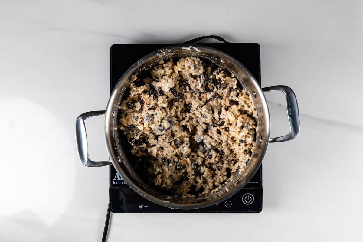 A metal pot with handles sits on a black electric stovetop, filled with a mixture of rice and black beans on a white countertop.