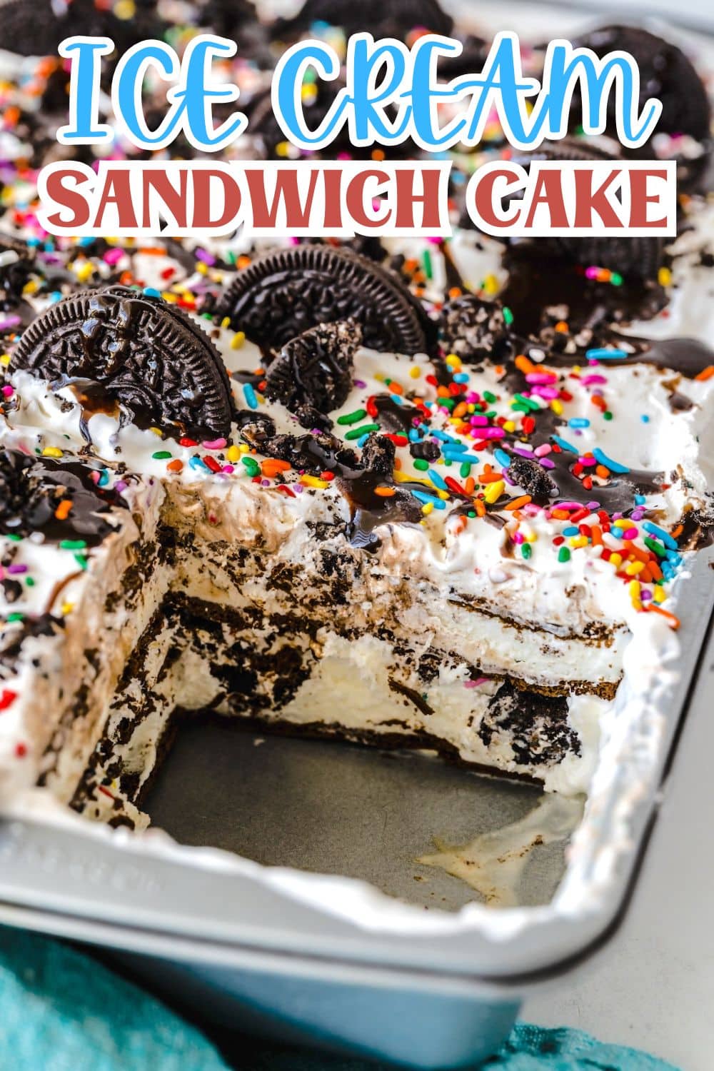 A pan of ice cream sandwich cake topped with whipped cream, rainbow sprinkles, and chocolate sandwich cookies, with a large square piece missing to reveal layers inside. Text at the top reads Ice Cream Sandwich Cake.