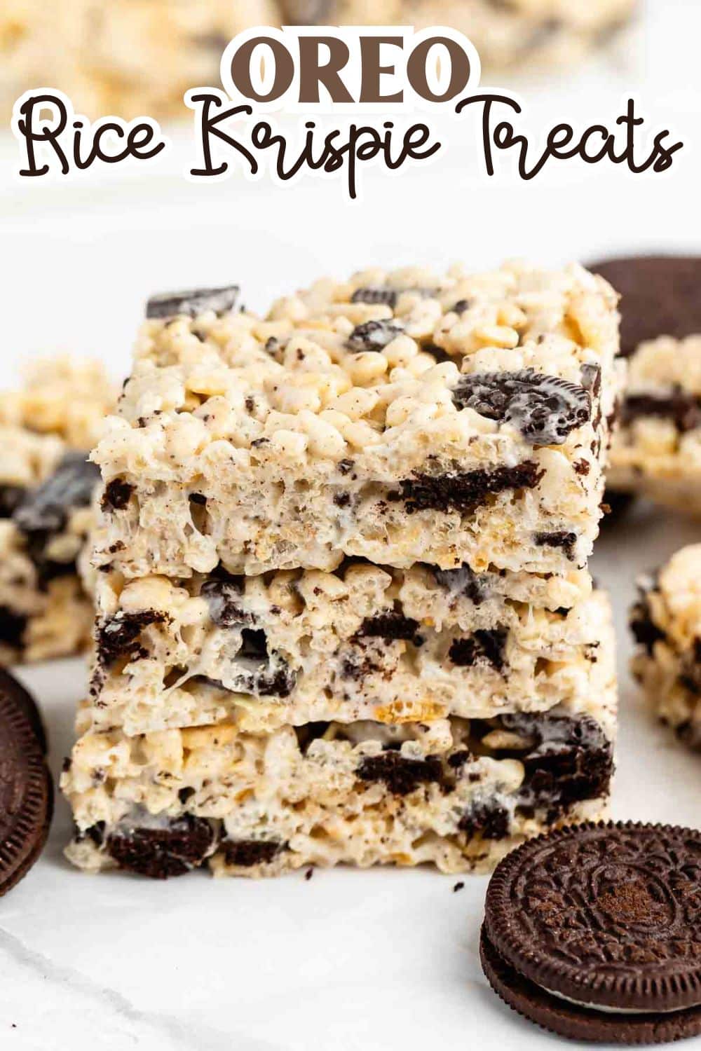 Three stacked Oreo Rice Krispie treats with visible Oreo cookie pieces, surrounded by additional treats and whole Oreo cookies on a white surface. The text Oreo Rice Krispie Treats is at the top.