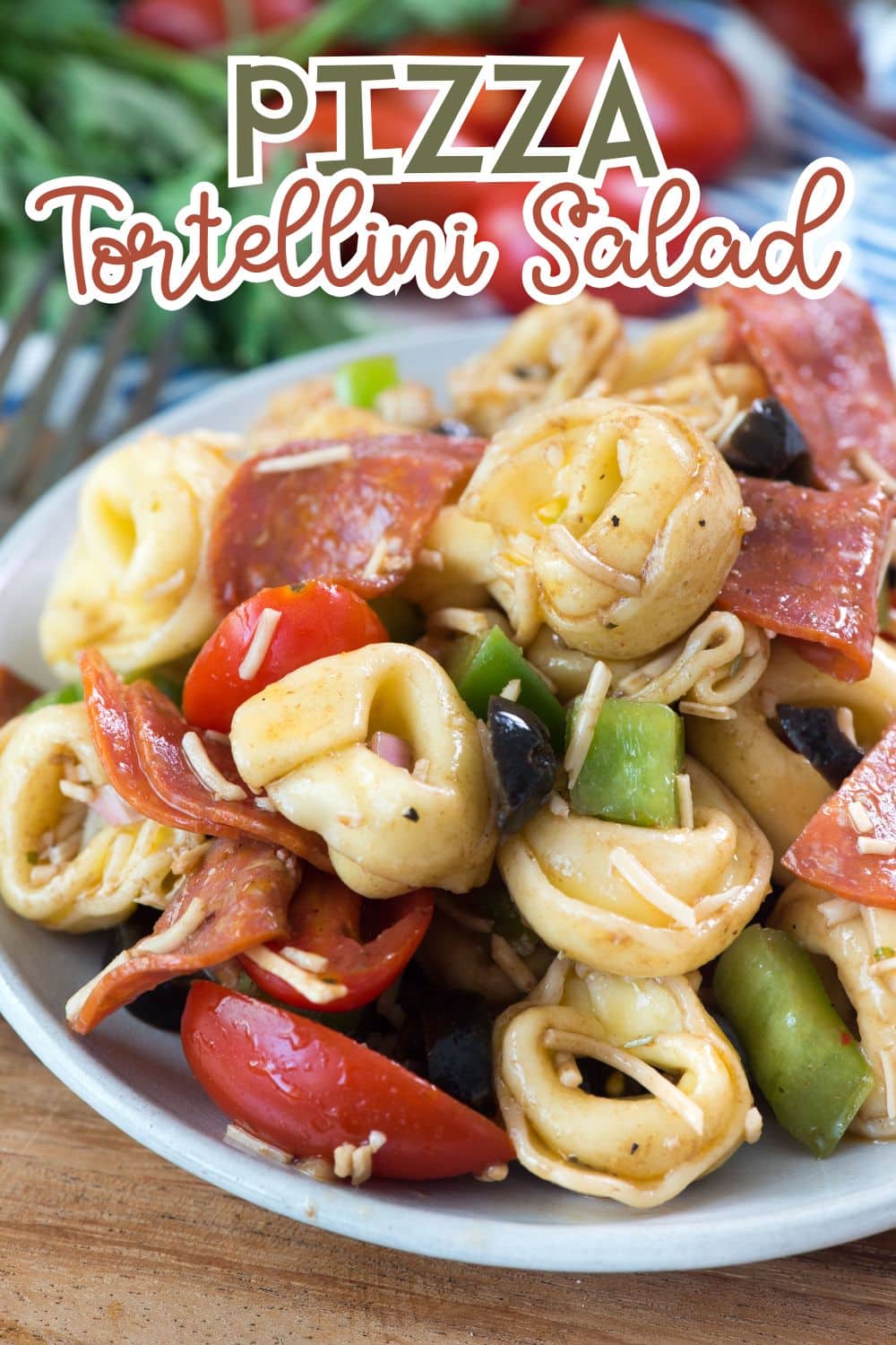 A bowl of pizza tortellini salad with cheese tortellini, pepperoni slices, cherry tomatoes, green peppers, black olives, and shredded cheese. Text on image reads PIZZA Tortellini Salad.