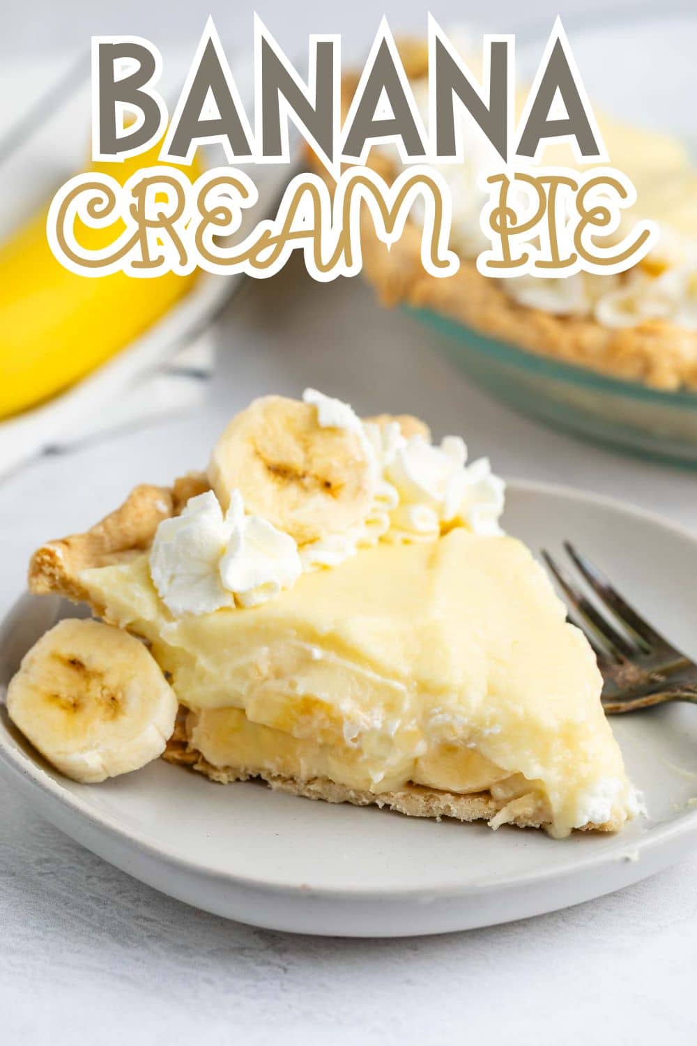 A slice of banana cream pie topped with whipped cream and banana slices on a plate with a fork; whole pie and banana in the background. Text at the top reads “BANANA CREAM PIE.”.