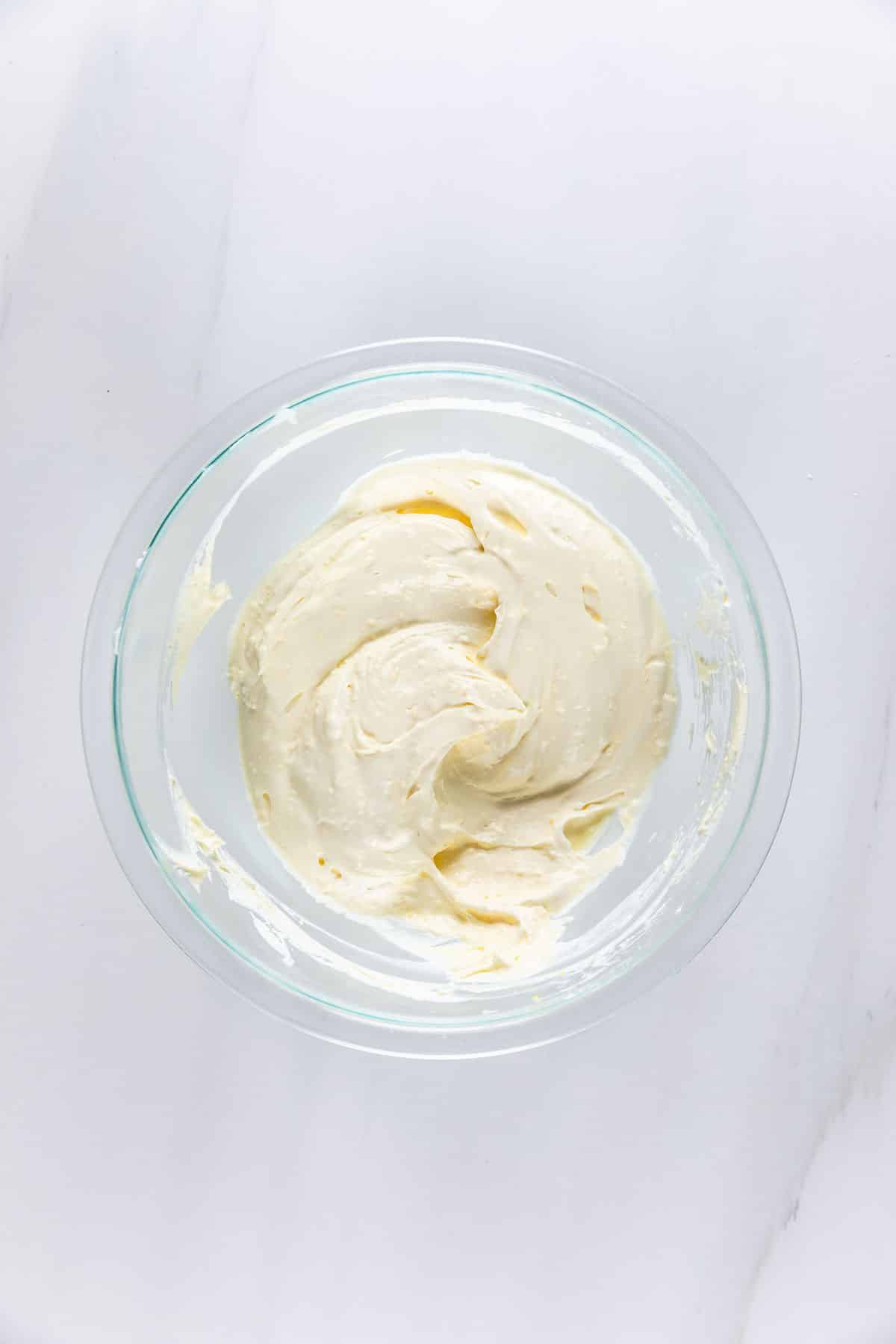 A glass bowl filled with creamy, pale yellow frosting or batter, placed on a white marble surface.