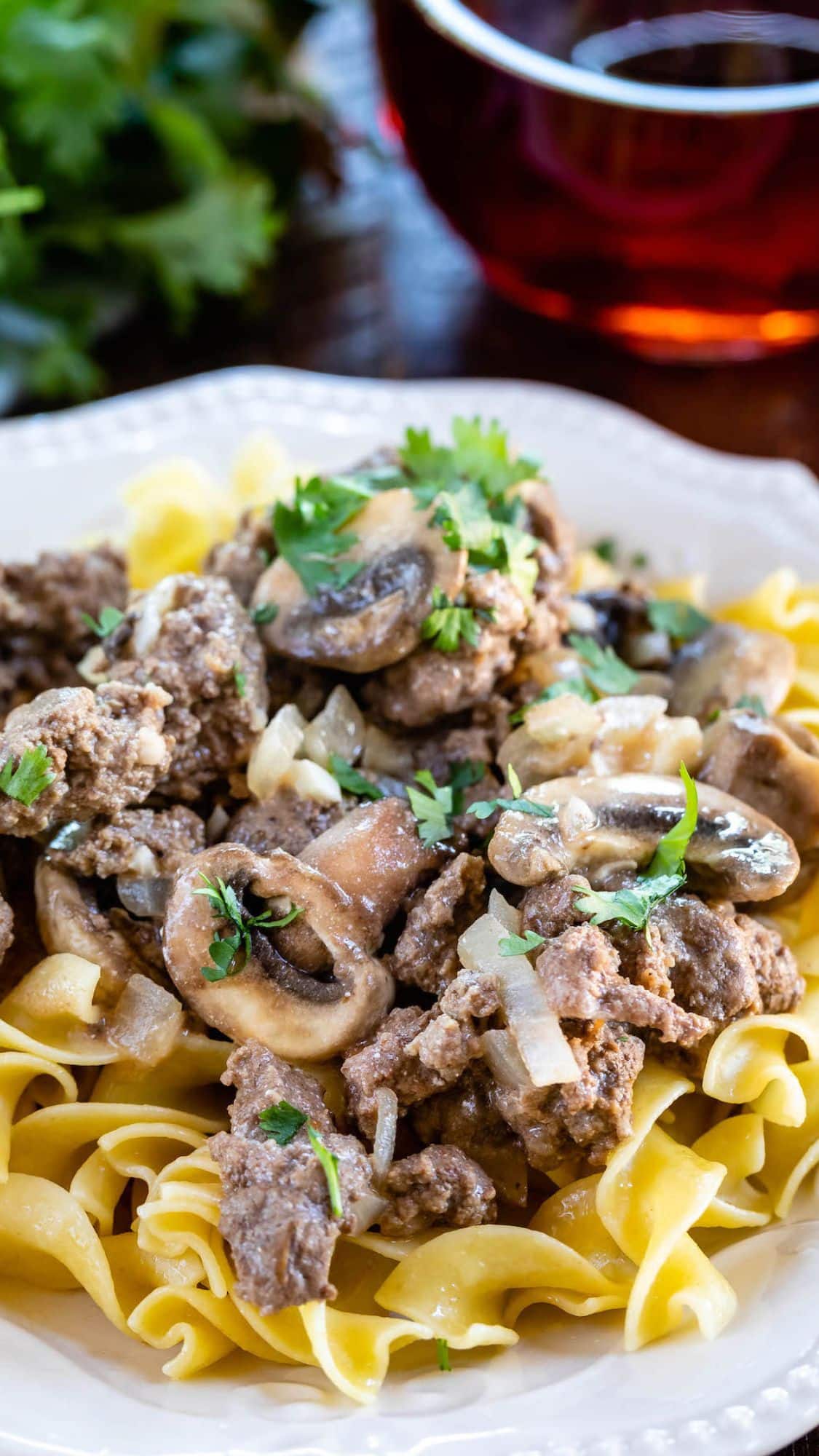 A plate of egg noodles topped with beef, sautรฉed mushrooms, onions, and fresh parsley, served on a white dish.