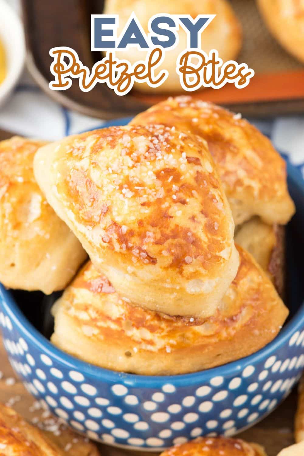 A blue and white polka dot bowl filled with golden-brown pretzel bites topped with coarse salt. Text at the top reads Easy Pretzel Bites in bold and cursive fonts.