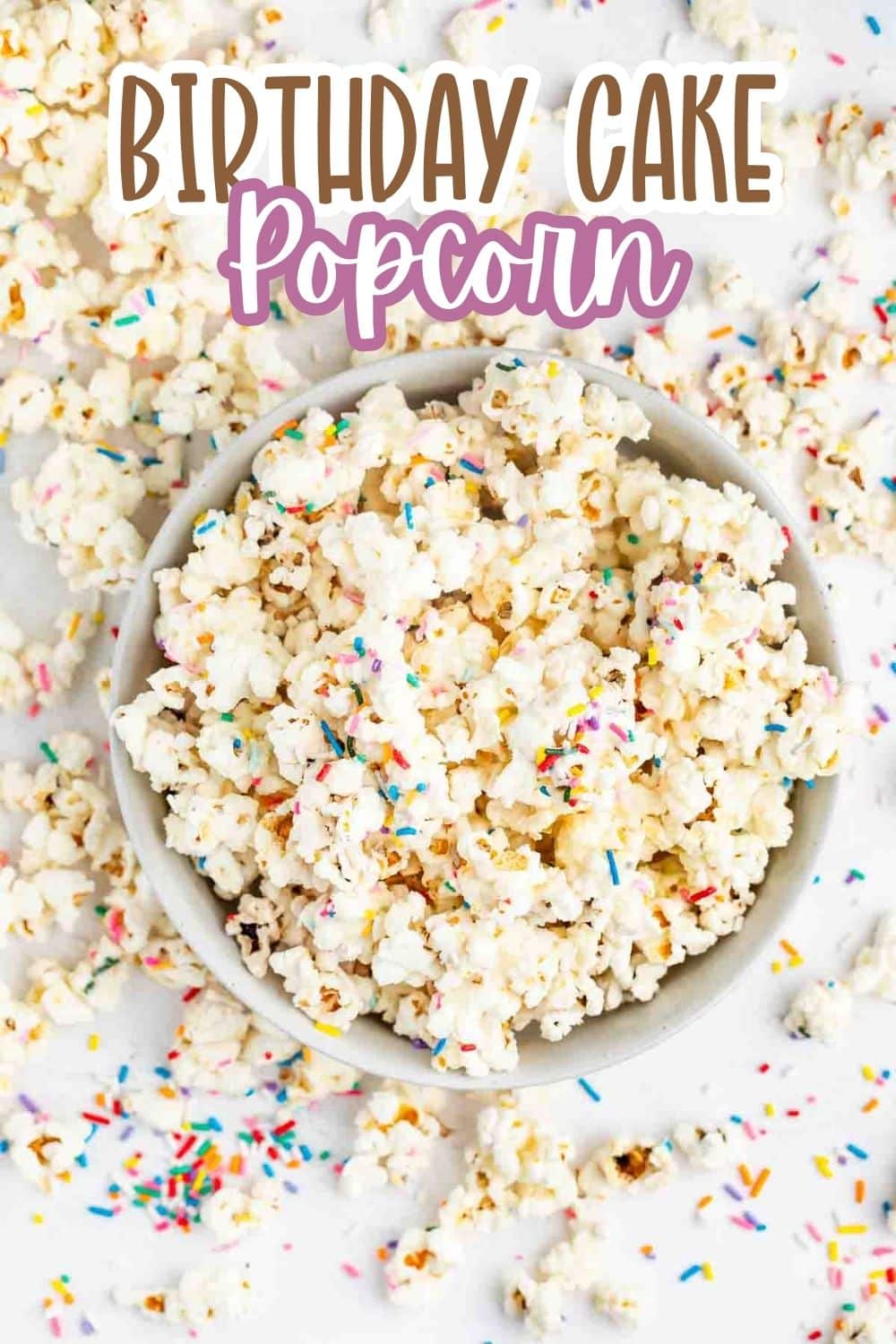 A bowl of popcorn covered in colorful sprinkles sits on a white surface scattered with more popcorn and sprinkles. Text above the bowl reads BIRTHDAY CAKE Popcorn.