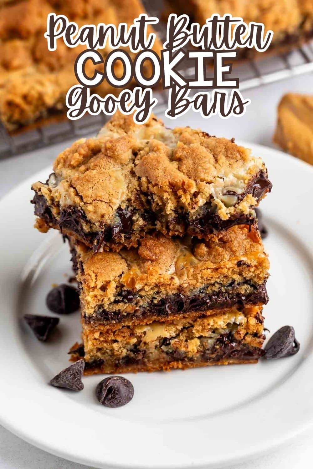 A stack of gooey peanut butter cookie bars with chocolate chips on a white plate, topped with chunks of cookies. The text Peanut Butter Cookie Gooey Bars is written above the bars.