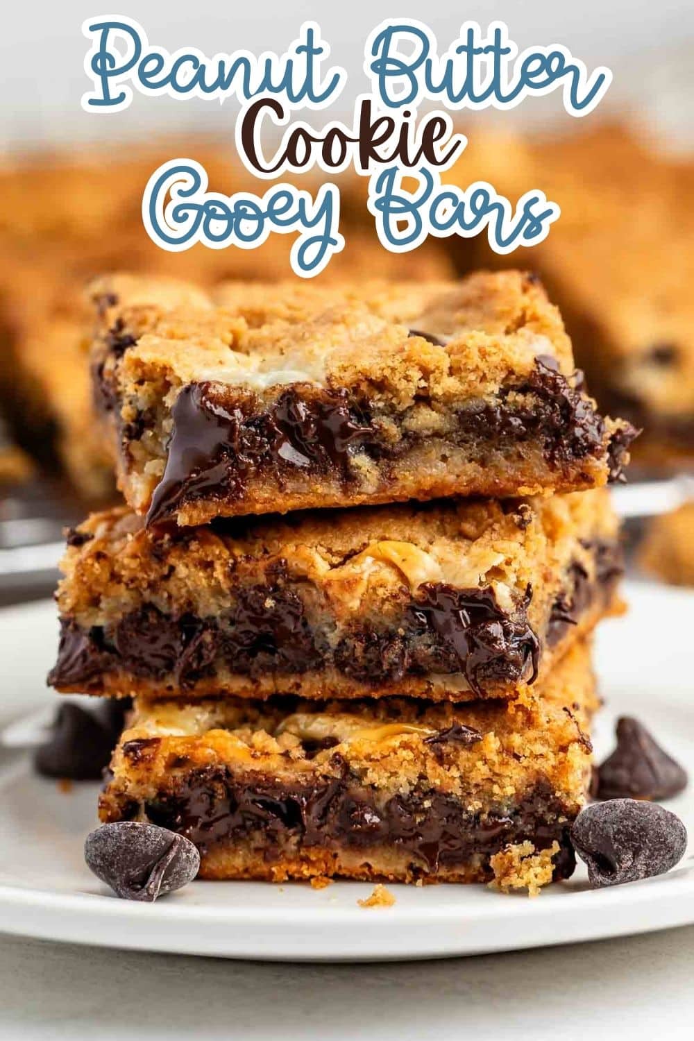 A stack of three peanut butter cookie bars filled with gooey melted chocolate, on a white plate with chocolate chips. The text above reads Peanut Butter Cookie Gooey Bars.