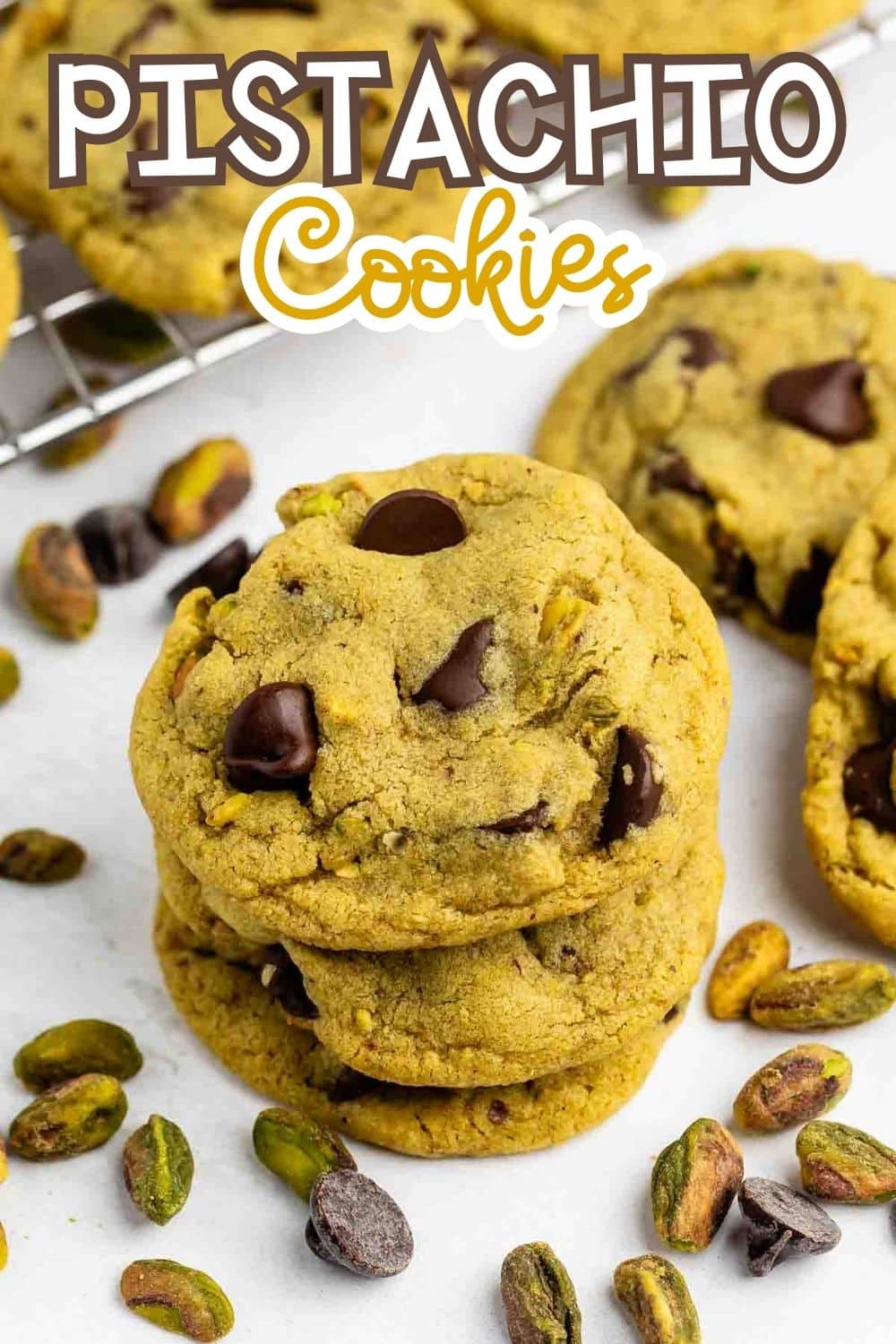 A stack of pistachio cookies with chocolate chips, surrounded by scattered pistachio nuts. More cookies are in the background on a cooling rack. The text Pistachio Cookies is written at the top of the image.