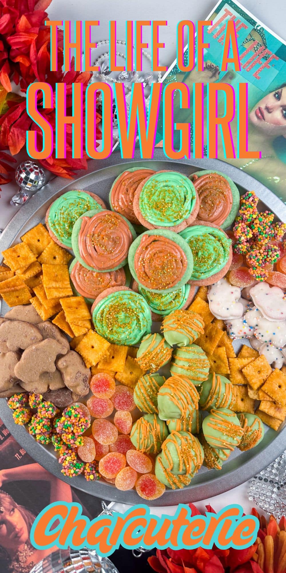 A colorful platter with cheese crackers, frosted cookies, animal crackers, green and orange treats, and gummy candies. Magazines, a disco ball, and red flowers surround the plate. Text reads: The Life of a Showgirl Charcuterie.