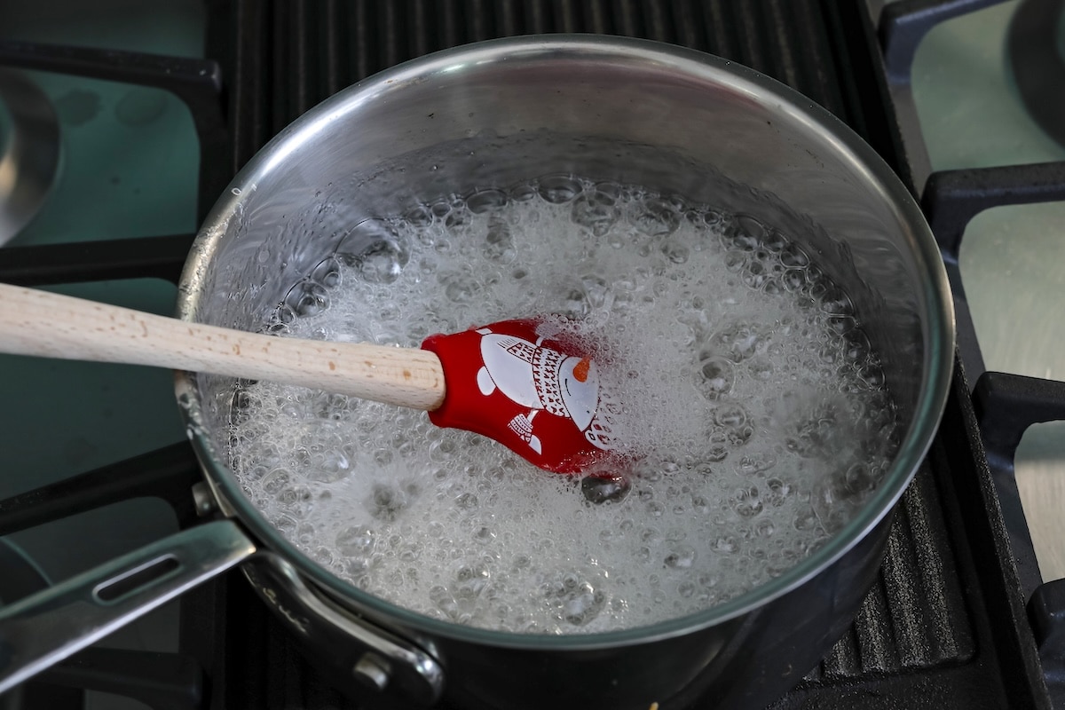 A red spatula stirs a bubbling, boiling liquid in a stainless steel pot on a gas stove.