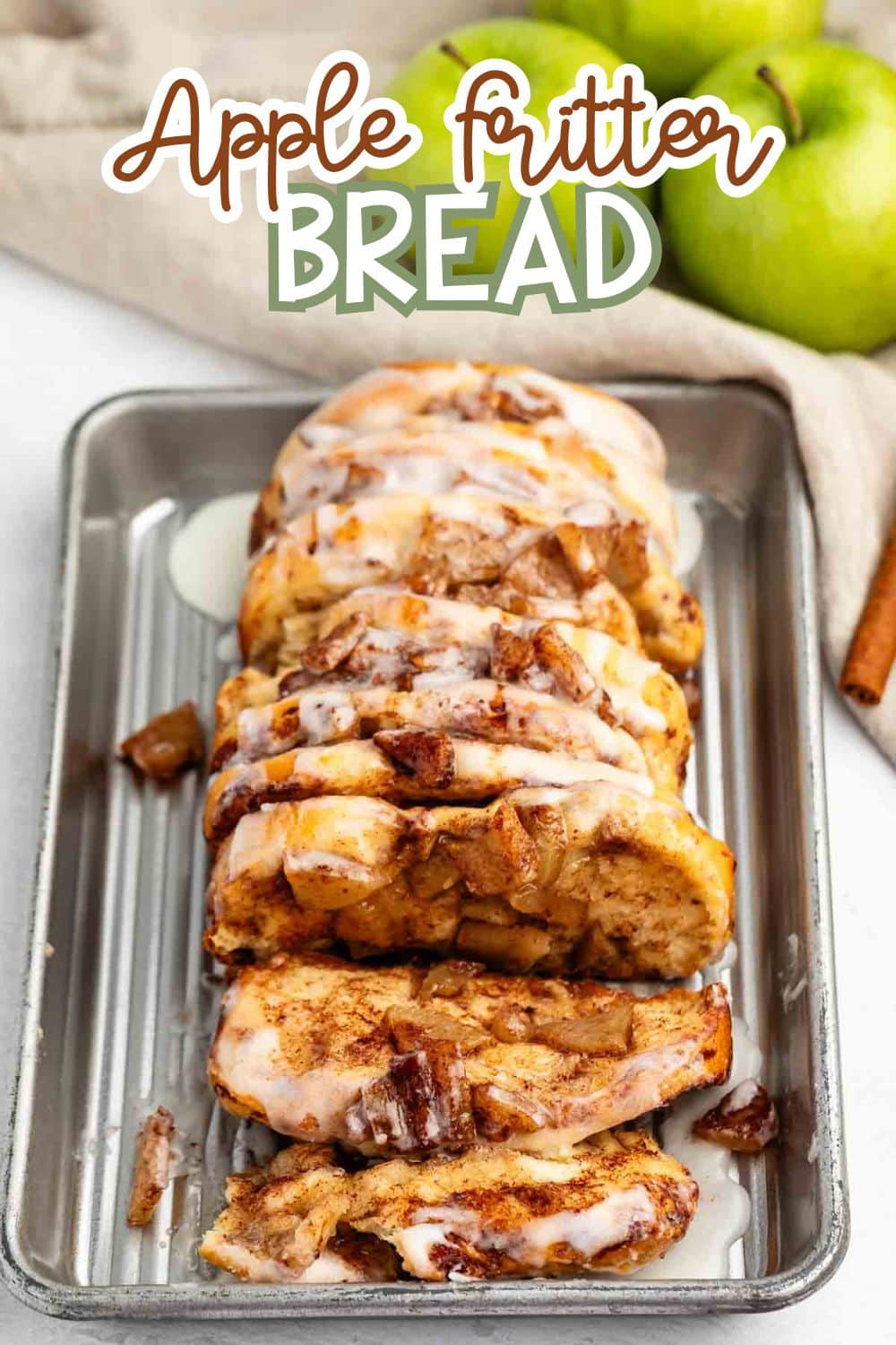 A loaf of apple fritter bread sliced and arranged on a metal tray, topped with white icing glaze. Two green apples and a cinnamon stick are in the background, with the text Apple Fritter Bread above.