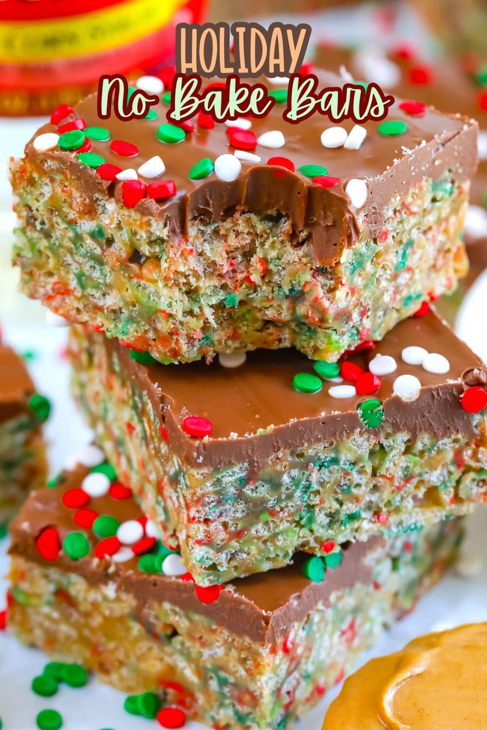 Three stacked holiday no-bake bars topped with chocolate and red, green, and white sprinkles. The bars have a chewy, colorful interior, and one has a bite taken out. Text on the image reads Holiday No Bake Bars.
