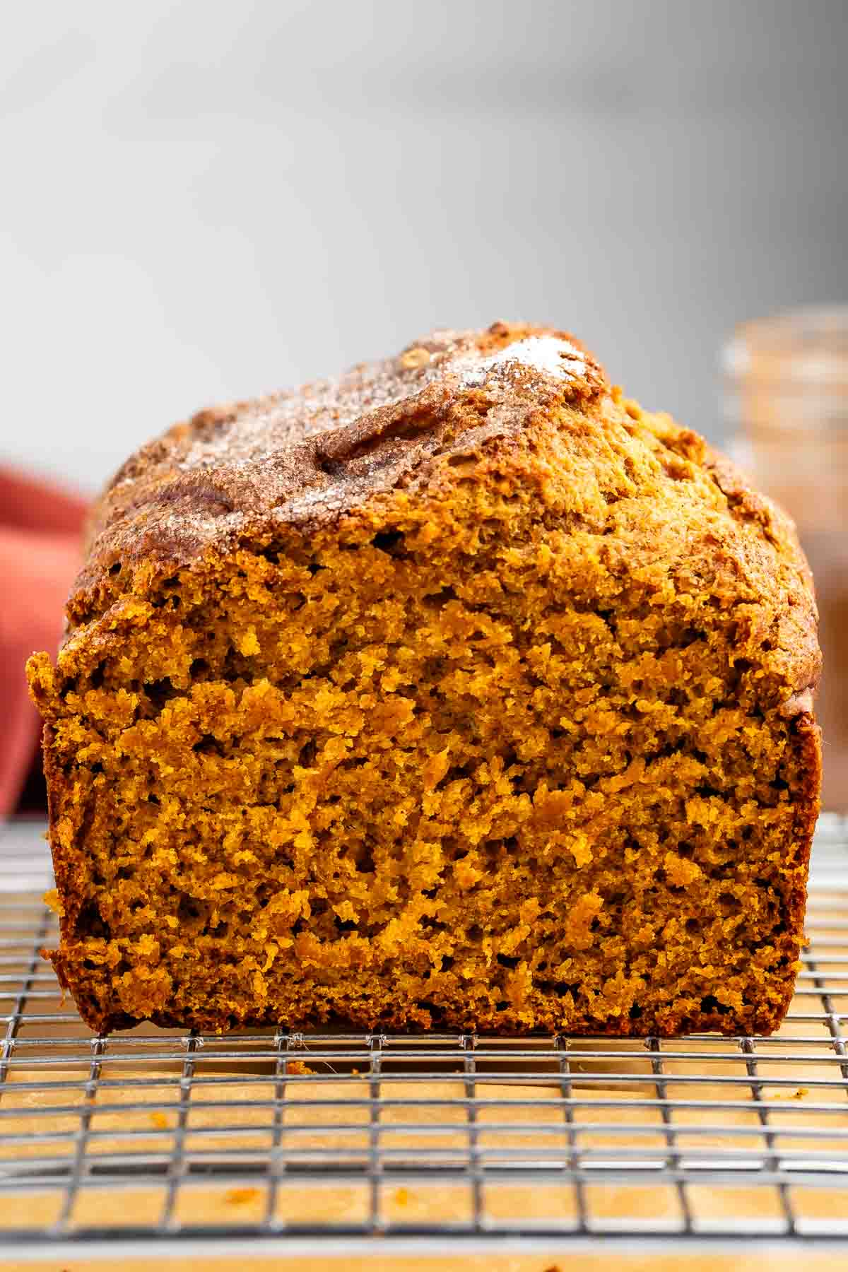 A loaf of pumpkin bread is shown on a cooling rack, sliced to display its moist, orange interior