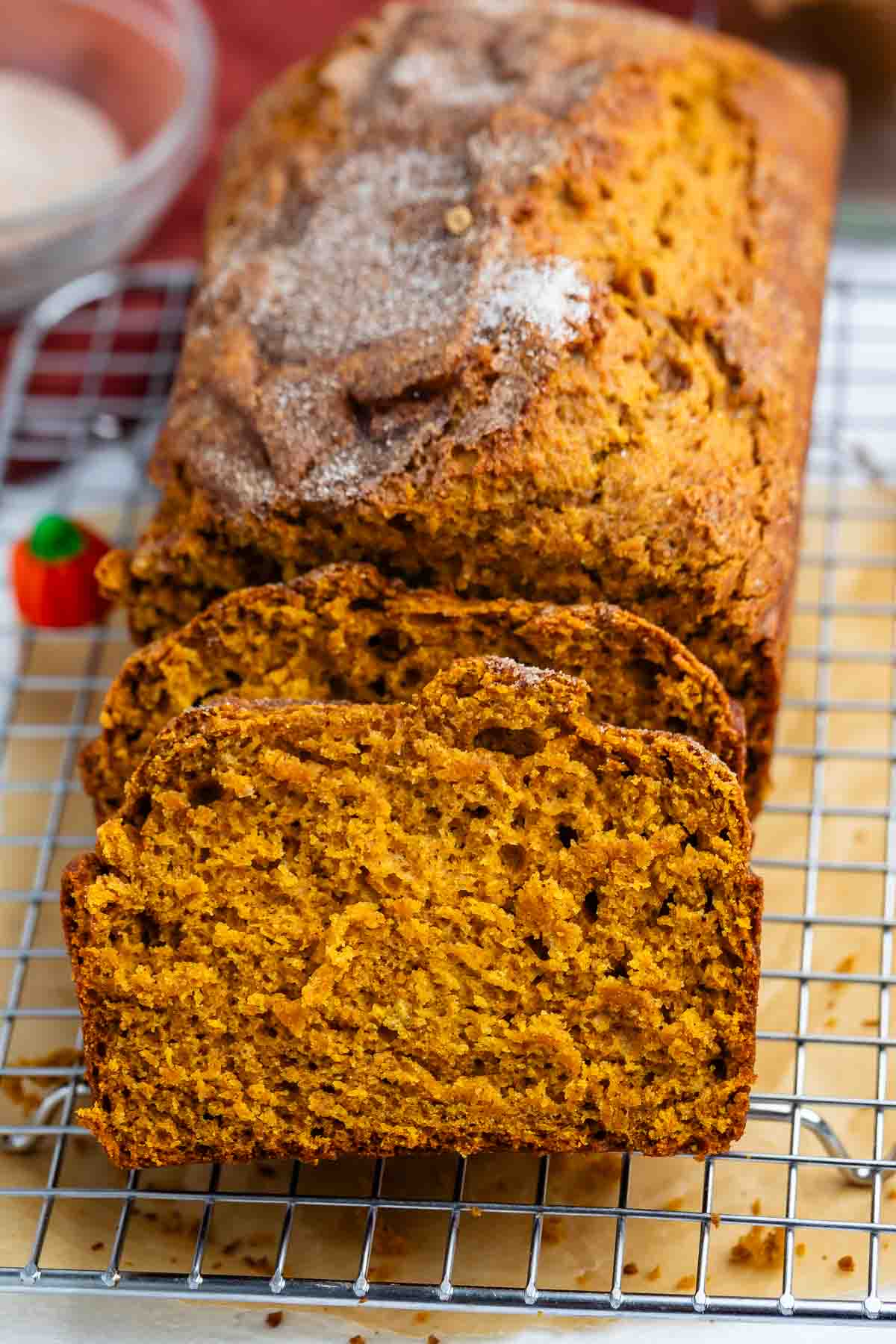 A loaf of pumpkin bread is shown on a cooling rack, sliced to display its moist, orange interior