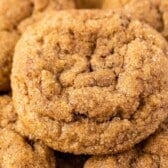 A close-up of several soft, round, golden-brown pumpkin snickerdoodles coated in cinnamon and sugar, showing a slightly cracked surface.
