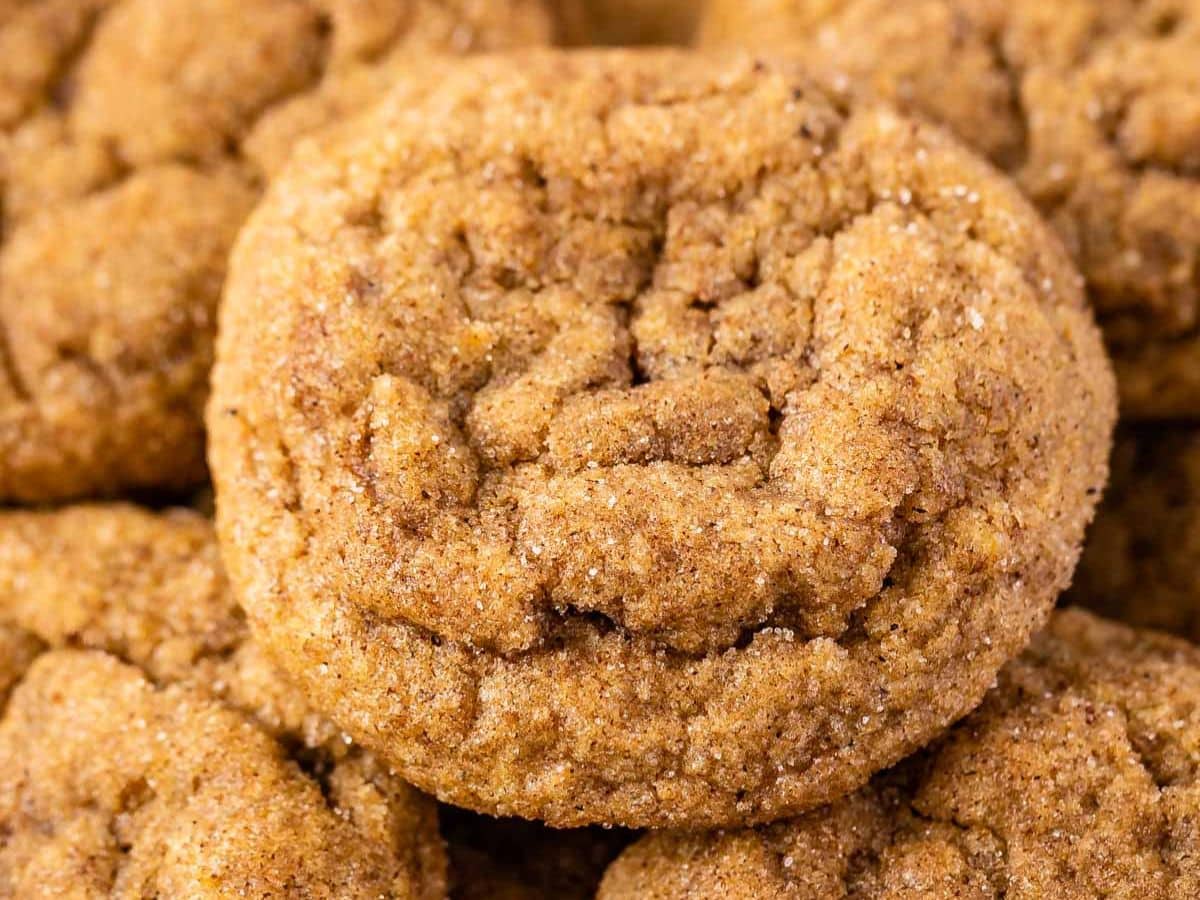 A close-up of several soft, round, golden-brown pumpkin snickerdoodles coated in cinnamon and sugar, showing a slightly cracked surface.