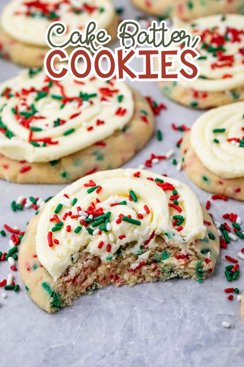 A frosted cookie with red and green sprinkles has a bite taken out of it. More cookies decorated the same way are in the background. Text above reads Cake Batter Cookies.