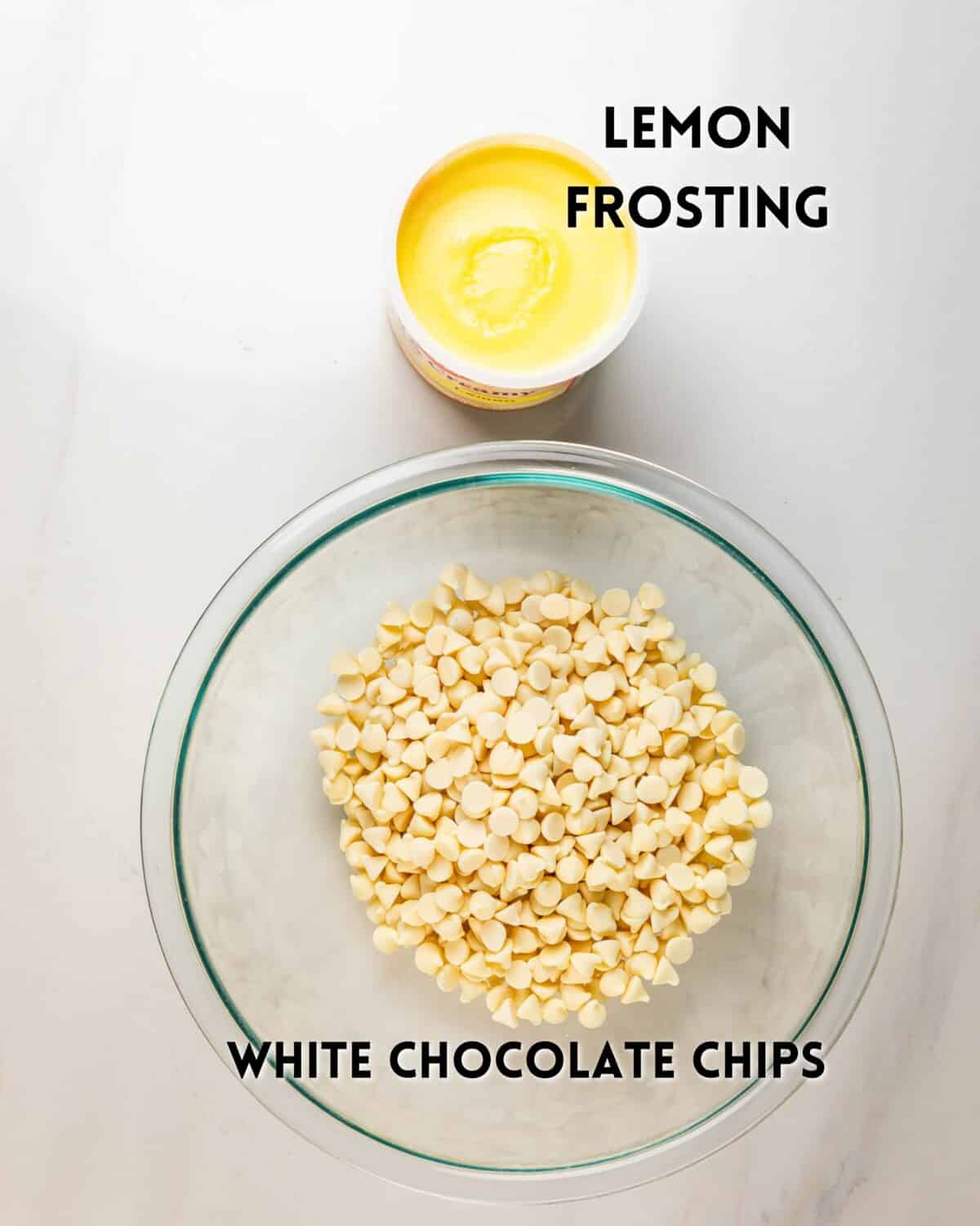 A glass bowl filled with white chocolate chips sits below a small tub of lemon frosting on a white surface. Both ingredients are labeled with text.