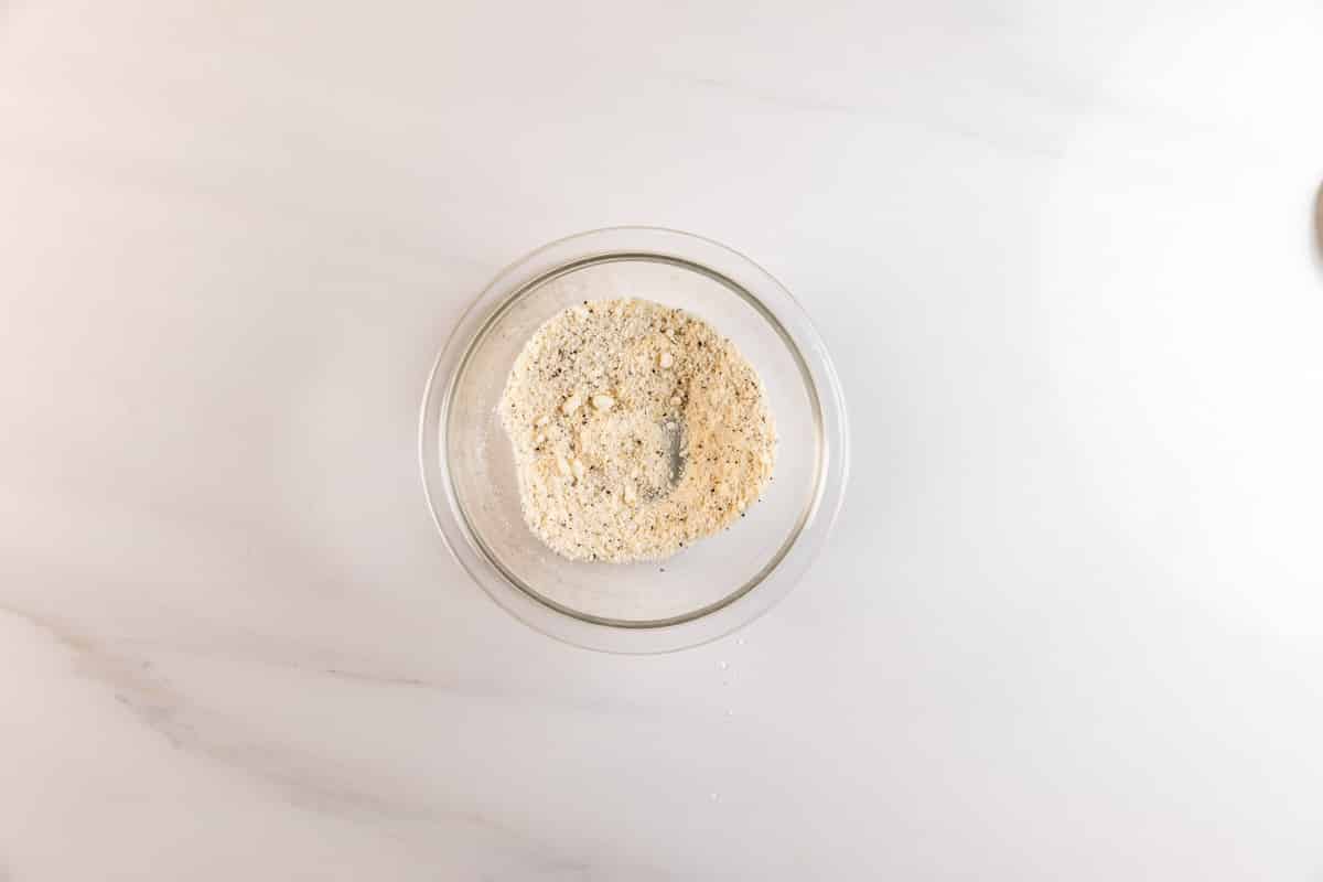 A glass bowl filled with a light beige, powdery mixture sits on a white marble surface.