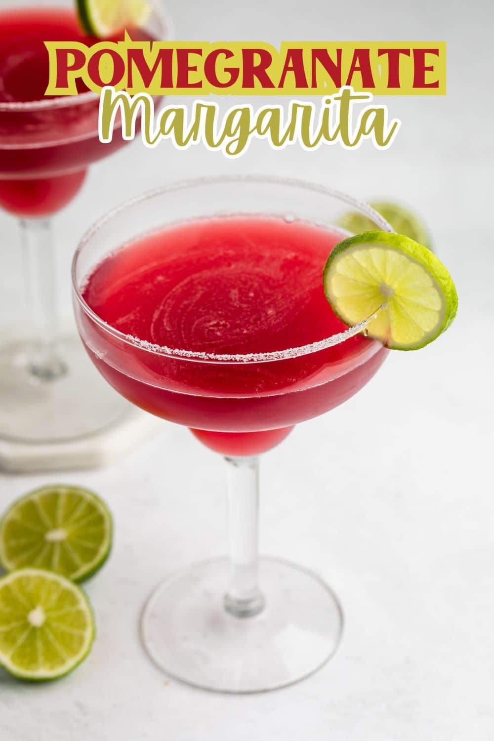 A pomegranate margarita in a salt-rimmed glass garnished with a lime slice. Another margarita and sliced limes are in the background, with text reading Pomegranate Margarita at the top.