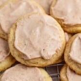 A close-up of several soft sugar cookies, inspired by Taylor Swift chai cookies, topped with a generous layer of cinnamon frosting and arranged closely together on a cooling rack.