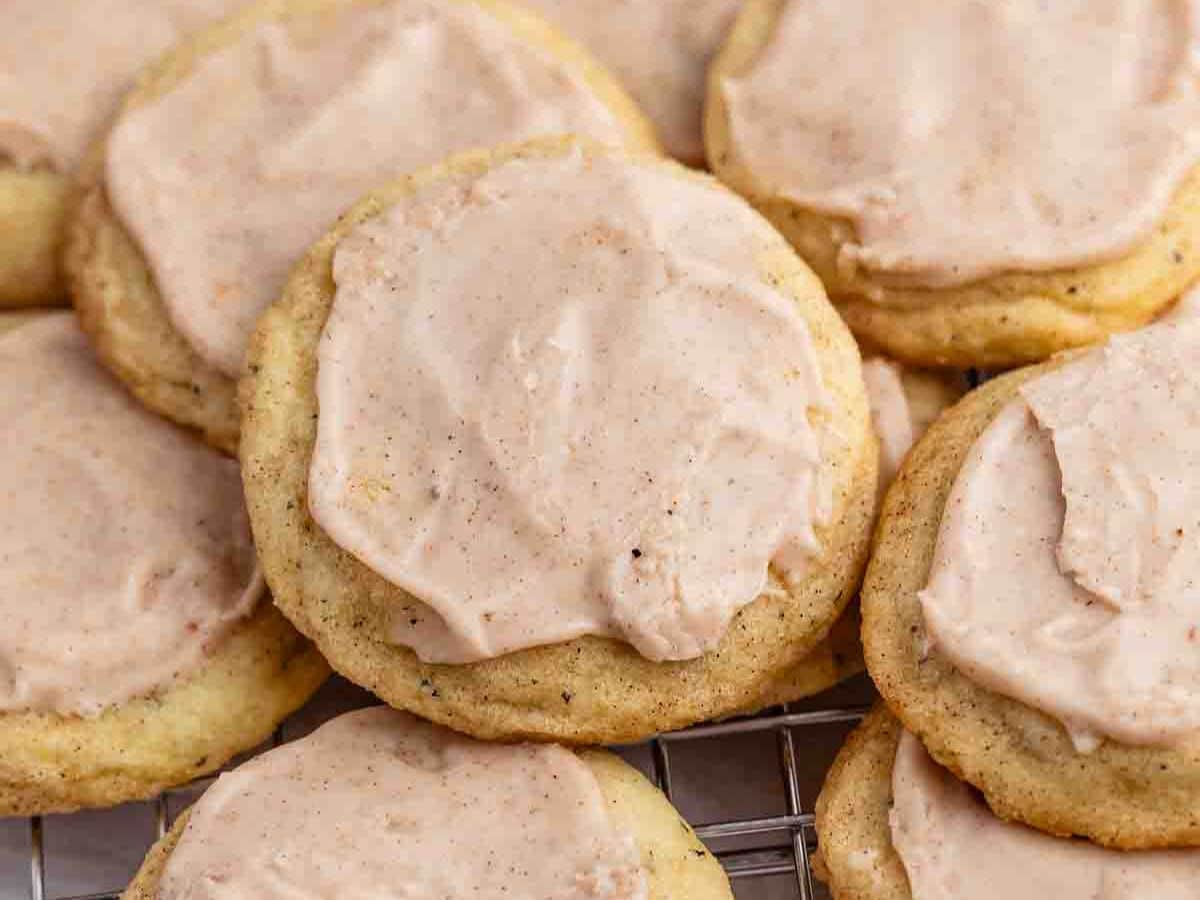 A close-up of several soft sugar cookies, inspired by Taylor Swift chai cookies, topped with a generous layer of cinnamon frosting and arranged closely together on a cooling rack.