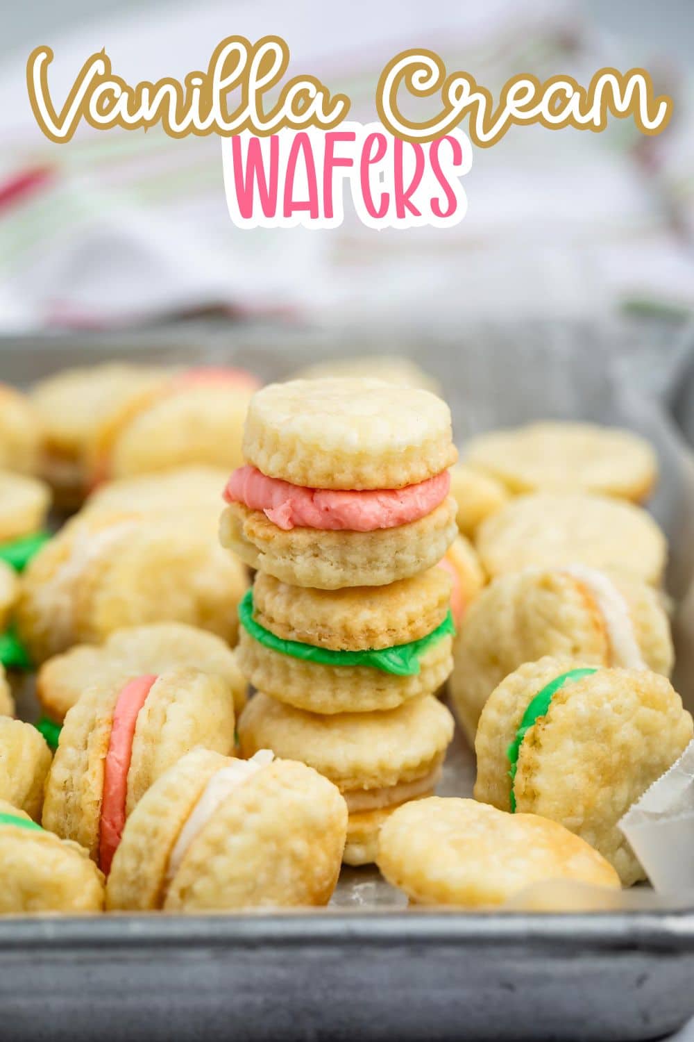 A tray filled with sandwich cookies made of round vanilla wafers and colorful cream fillings in pink and green. Text on the image reads Vanilla Cream Wafers.