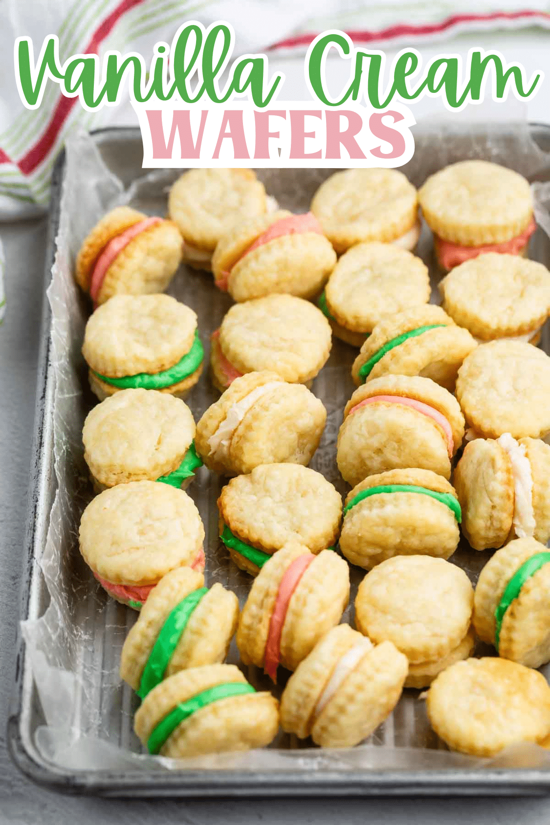 A tray lined with parchment paper holds rows of vanilla cream wafer sandwich cookies filled with pastel pink, green, and white cream. Vanilla Cream Wafers is written at the top in colorful text.