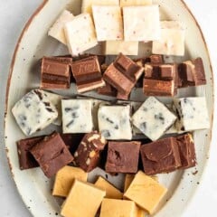 An oval plate holding rows of assorted fudge squares in different flavors and colors, including white, brown, and caramel, neatly arranged on a light background.